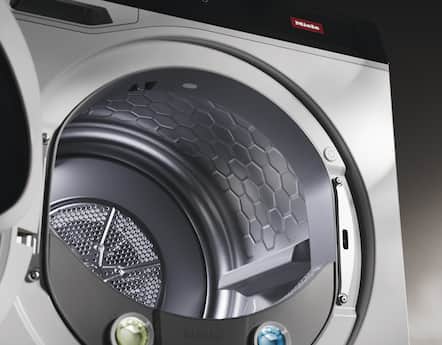 Close-up of a Miele front-load dryer interior, highlighting the honeycomb drum texture, lint filter, and open door for product detail.