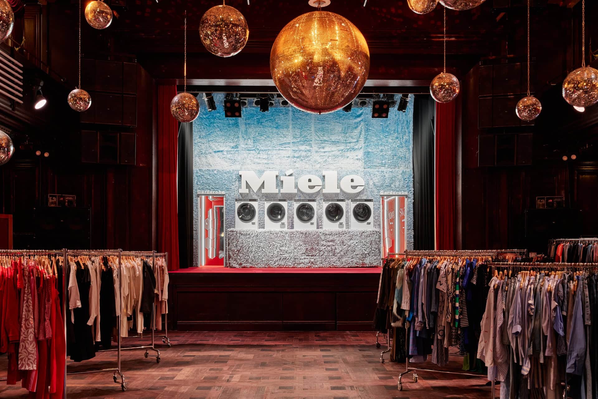 Stilvolle Event-Location mit Discokugeln und Kleiderständern; auf einer Bühne werden Miele-gebrandete Waschmaschinen vor einer glänzenden, schimmernden Kulisse präsentiert.