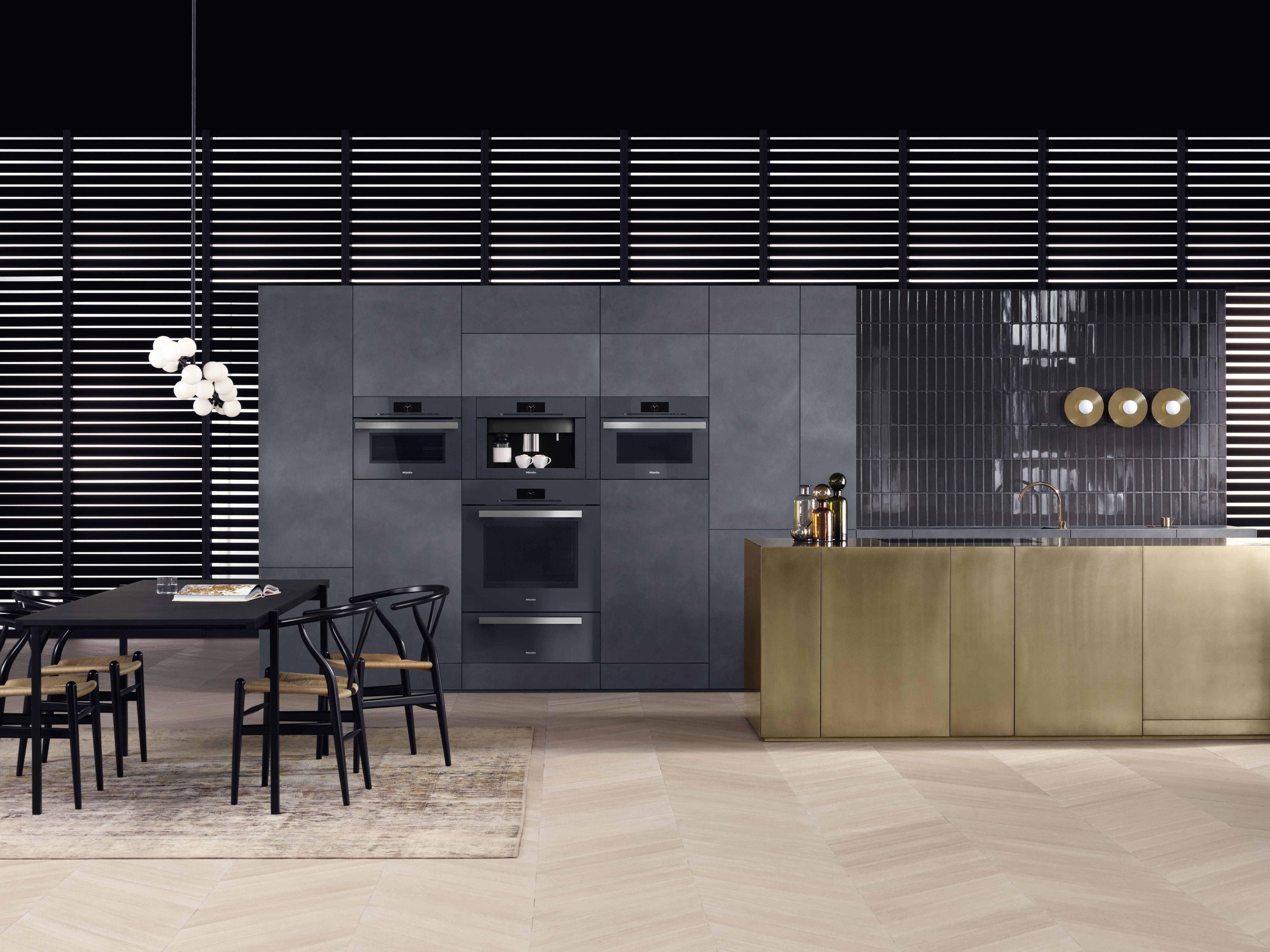 Cocina contemporánea con gabinetes gris oscuro y hornos y máquina de café integrados, una isla en tonos dorados con fregadero y una mesa de comedor con sillas negras. Cocina contemporánea con gabinetes gris oscuro y hornos y máquina de café integrados, una isla en tonos dorados con fregadero y una mesa de comedor con sillas negras.