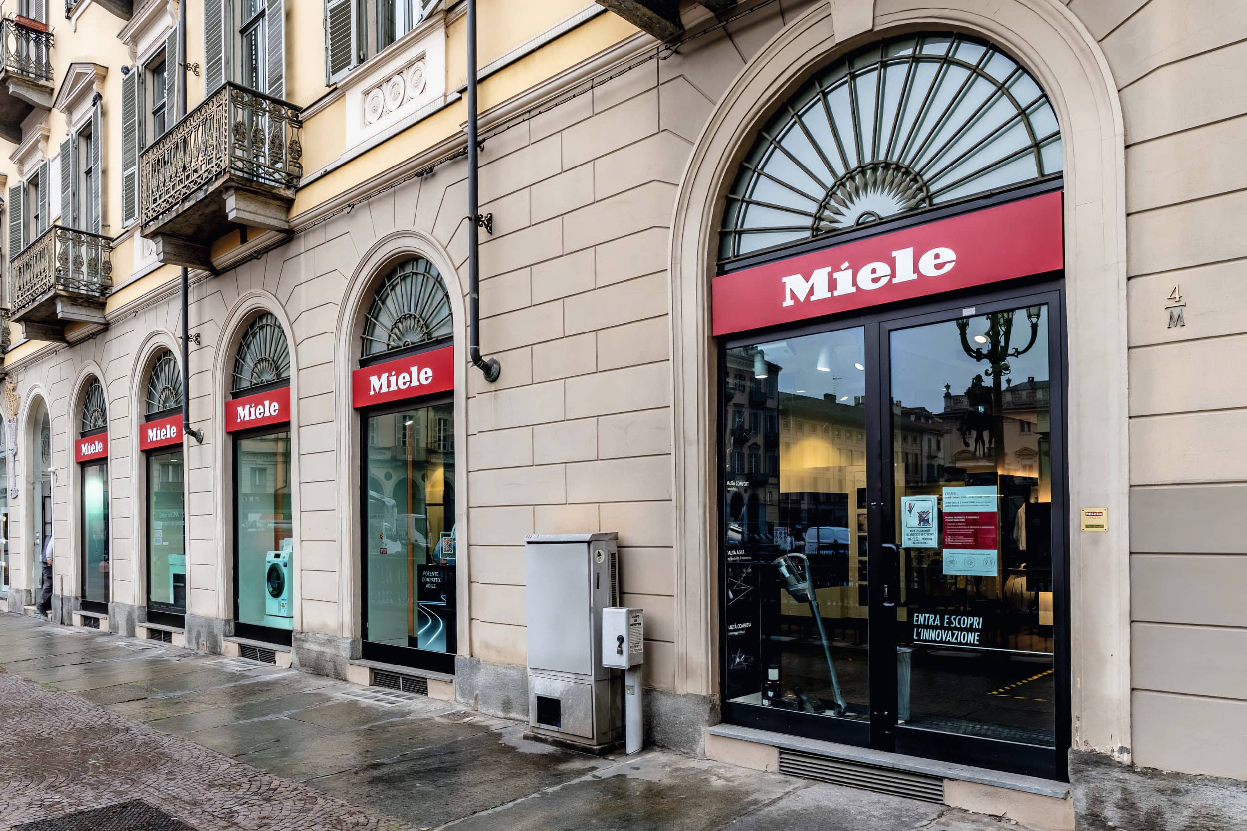 Vista della strada di uno showroom Miele in un edificio storico con finestre ad arco e insegne rosse. Vista della strada di uno showroom Miele in un edificio storico con finestre ad arco e insegne rosse.