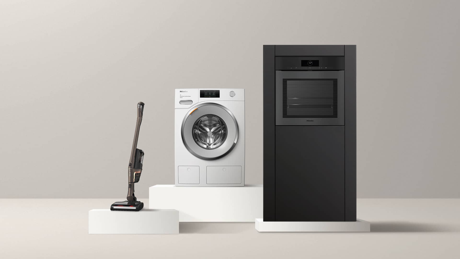 Un aspirateur balai sans fil, un lave-linge à chargement frontal et un four noir encastrable, présentés sur des socles minimalistes.