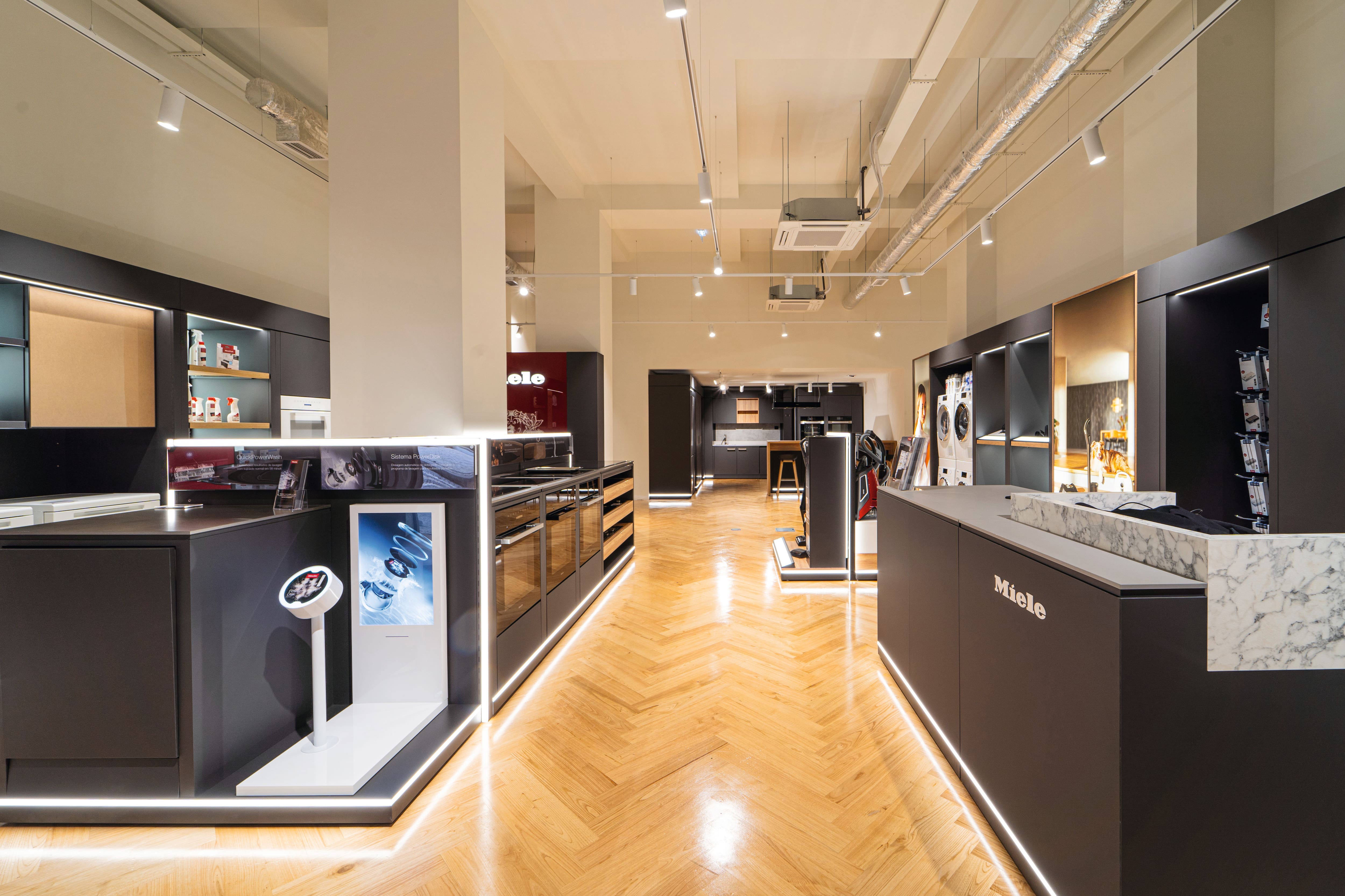 Showroom de eletrodomésticos modernos com expositores pretos elegantes, chão de madeira em espinha e cozinhas iluminadas. Showroom de eletrodomésticos modernos com expositores pretos elegantes, chão de madeira em espinha e cozinhas iluminadas.
