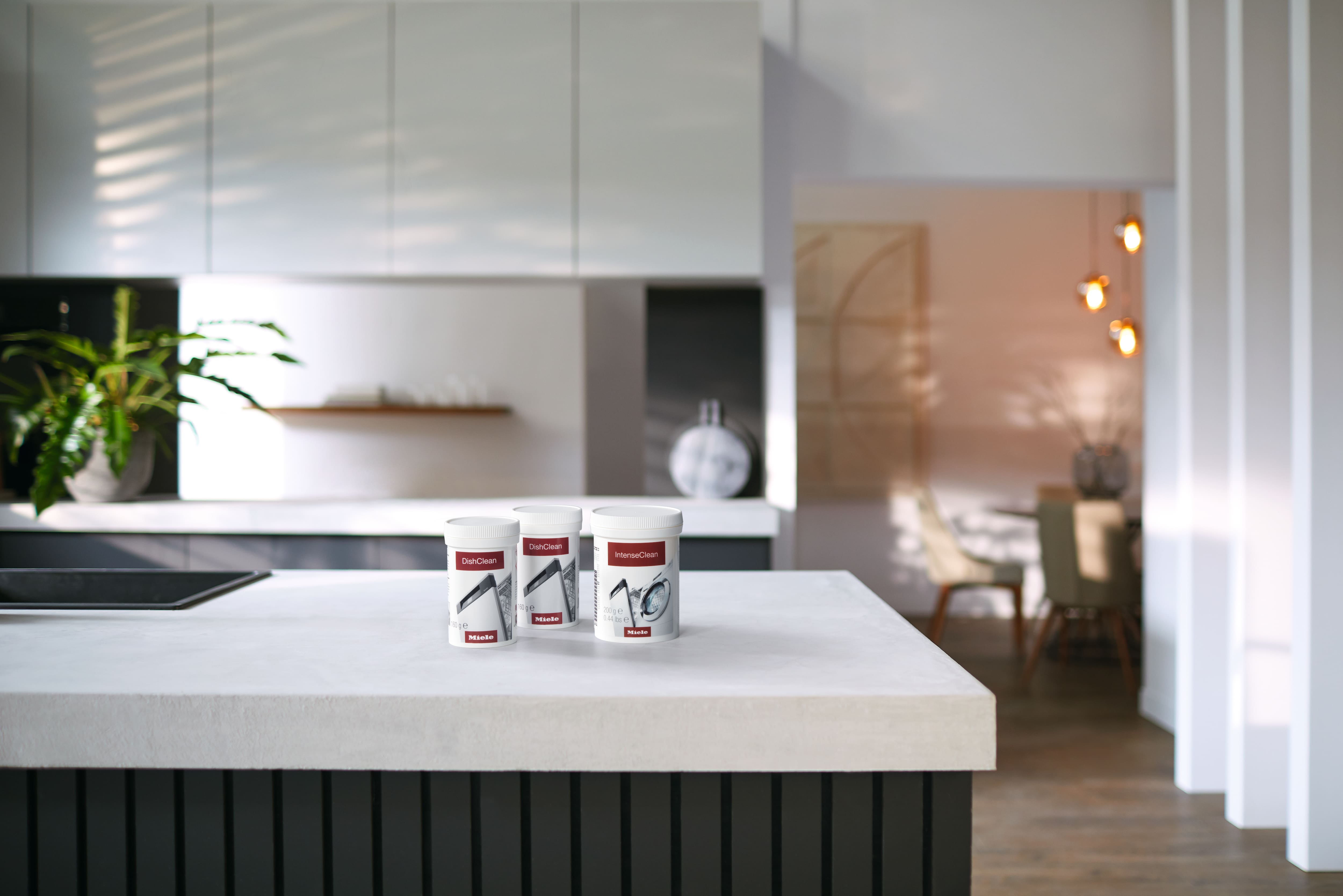 Three Miele DishClean and IntenseClean jars on a modern kitchen counter, showcasing appliance cleaning products.