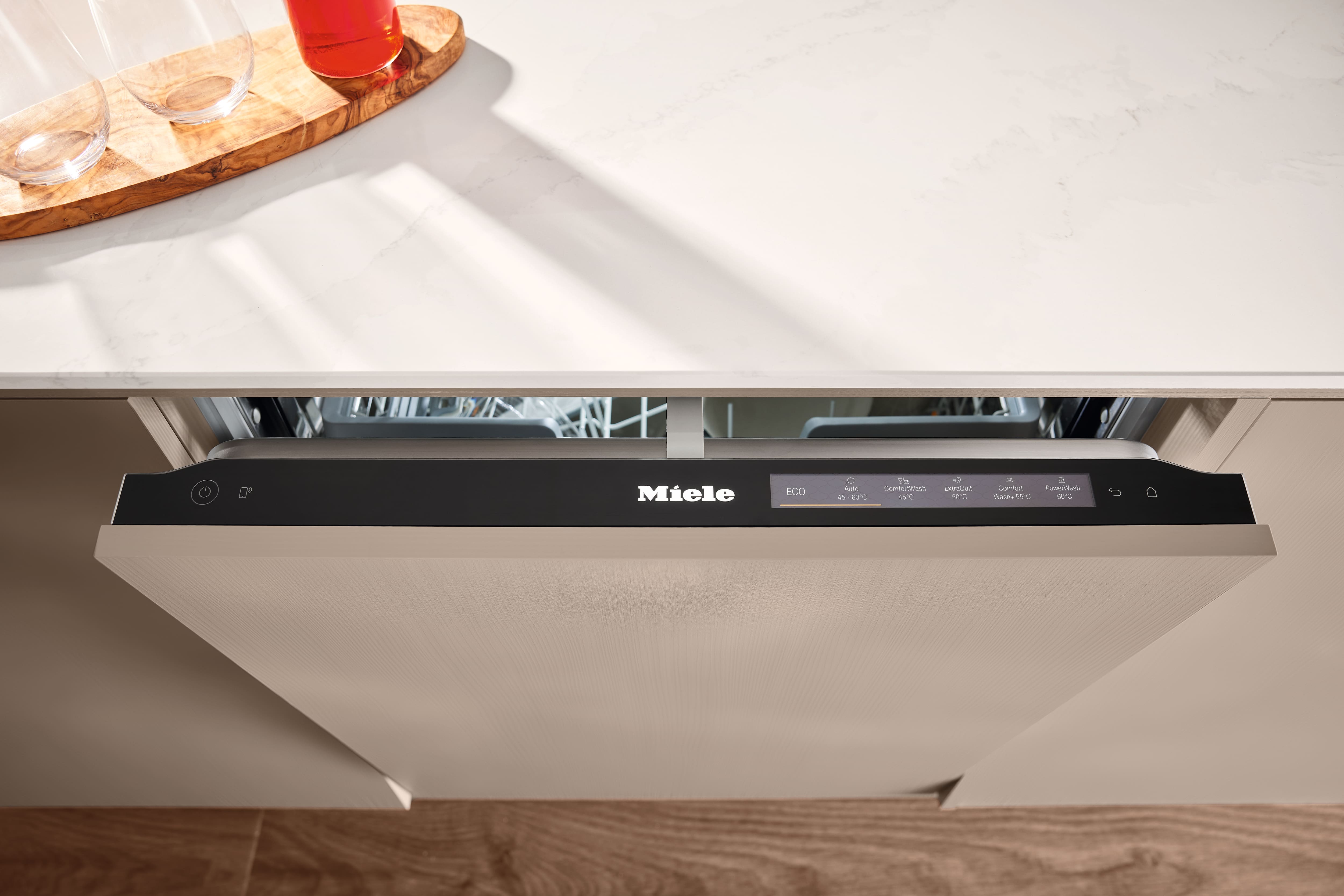 Integrated Miele dishwasher partially open under a marble countertop, showing black control panel and wash modes.