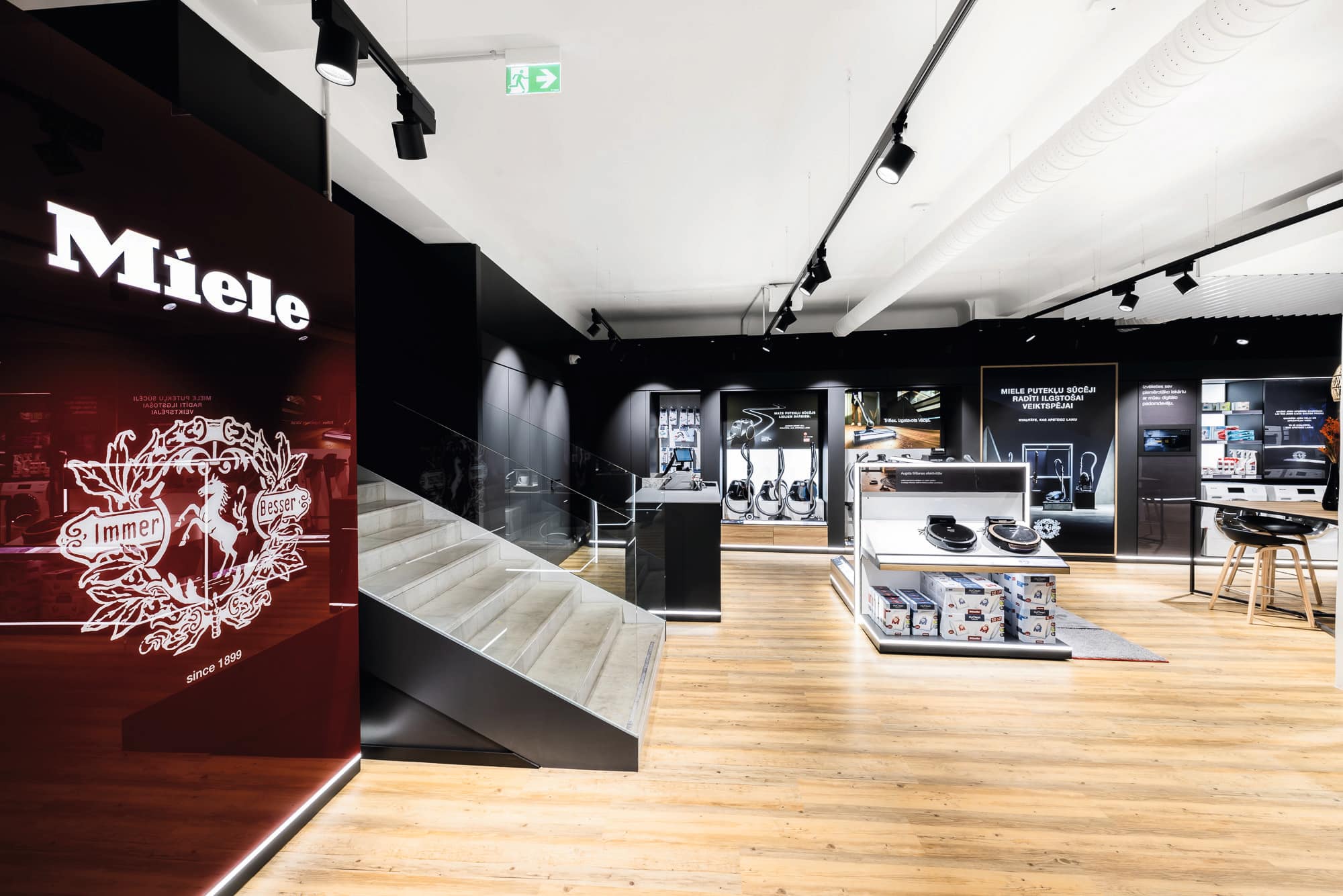 Mūsdienīgs Miele salons ar elegantu apgaismojumu, ierīču izstādēm un centrālajām kāpnēm gaišā tirdzniecības telpā. Mūsdienīgs Miele salons ar elegantu apgaismojumu, ierīču izstādēm un centrālajām kāpnēm gaišā tirdzniecības telpā.