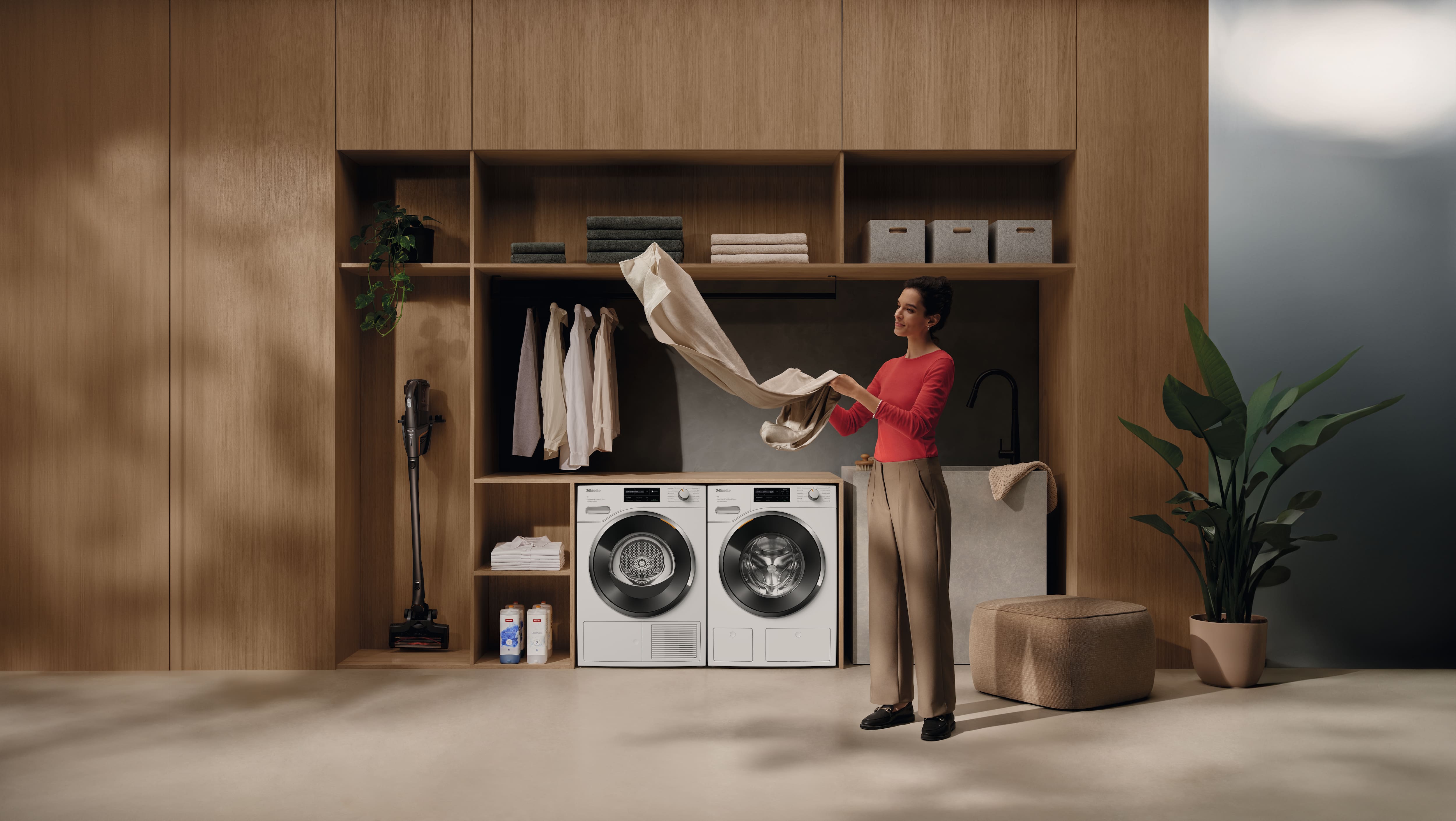 Moderne wasruimte met ingebouwde planken, wasmachine en droger, en een persoon die linnengoed vouwt naast een gootsteen. Moderne wasruimte met ingebouwde planken, wasmachine en droger, en een persoon die linnengoed vouwt naast een gootsteen.