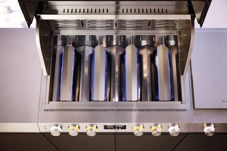 Open stainless steel gas grill with five blue-flame burners and illuminated knobs, heating to 250°C.