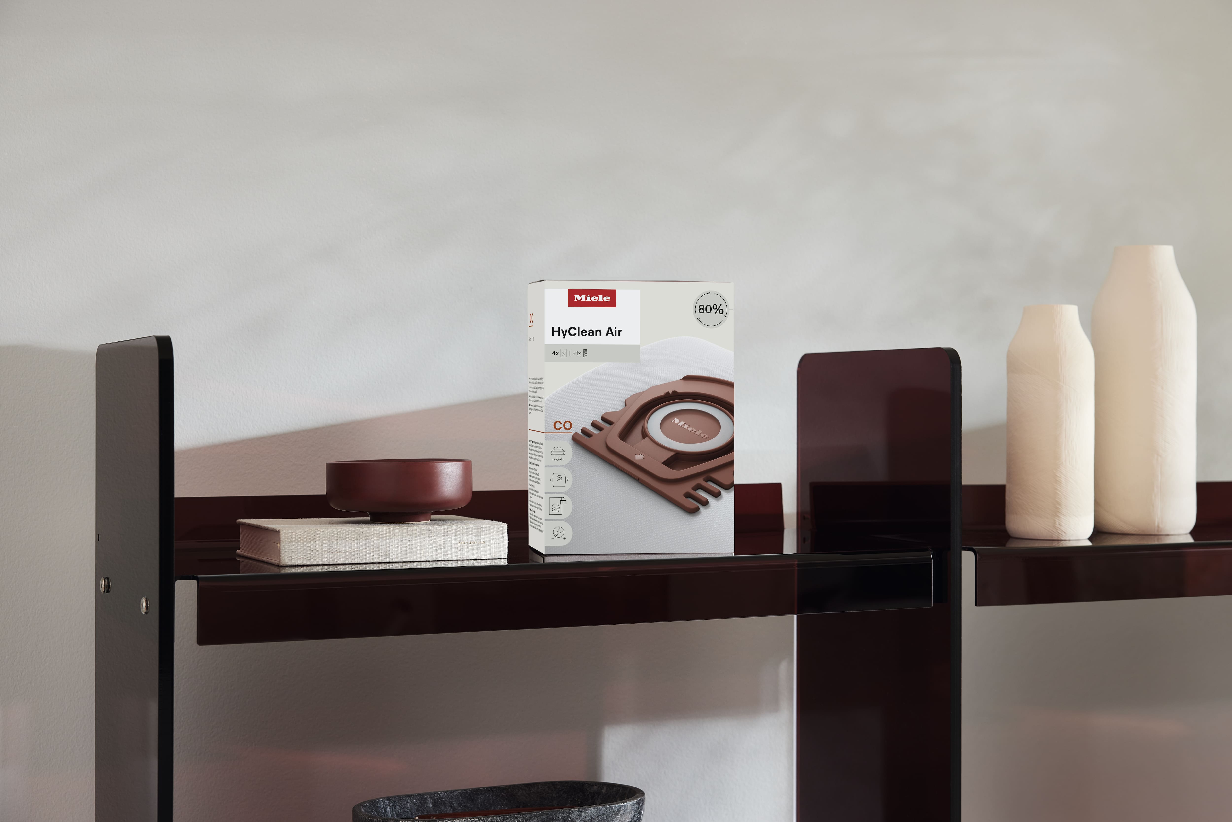 Miele HyClean Air vacuum bag box displayed on a minimalist shelf beside ceramic vases and a bowl, highlighting packaging. Miele HyClean Air vacuum bag box displayed on a minimalist shelf beside ceramic vases and a bowl, highlighting packaging.