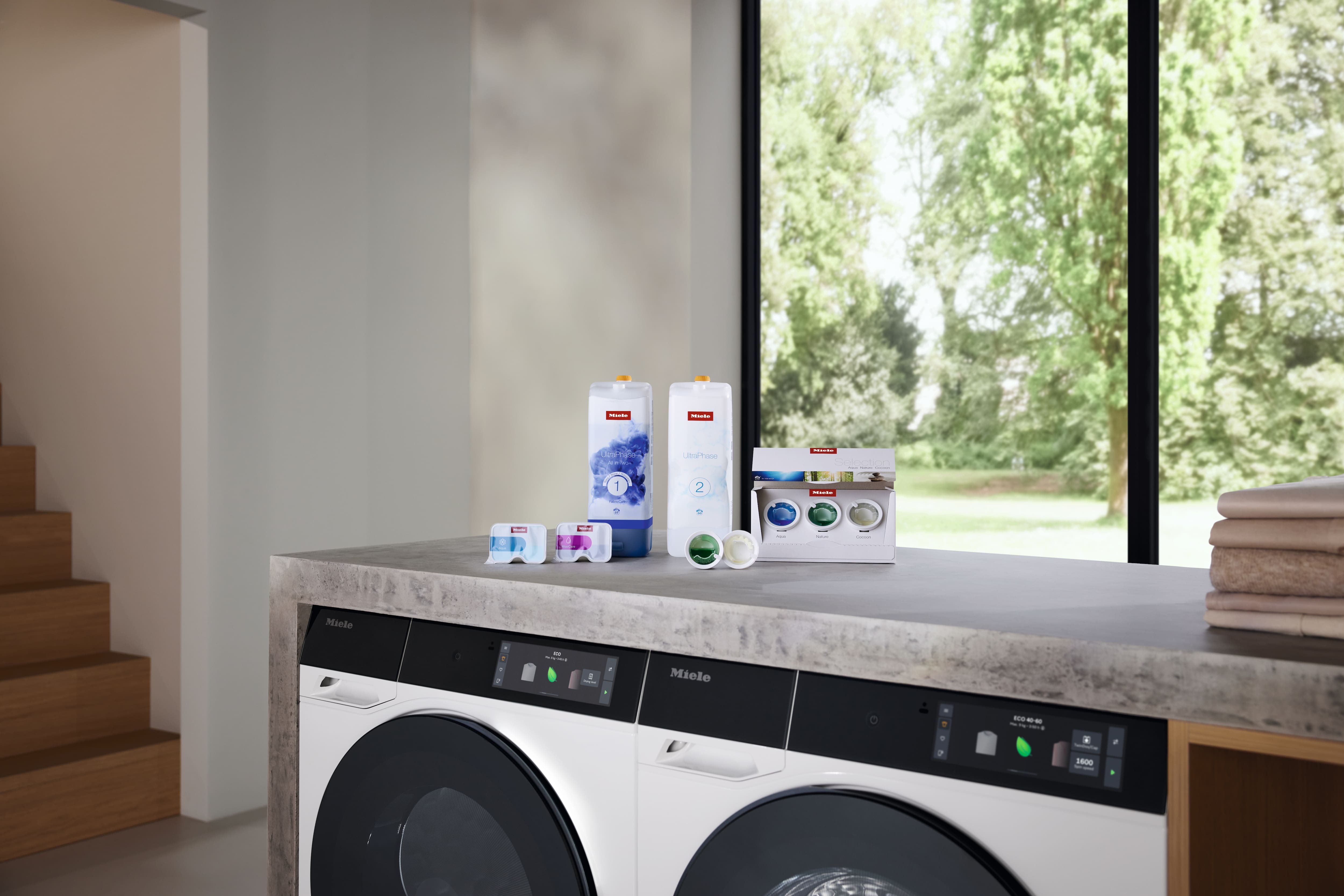 Lavatrice e asciugatrice Miele con detergenti UltraPhase e detersivo per lavastoviglie PowerDisk su un piano di lavoro in un moderno spazio abitativo inondato di luce naturale. Lavatrice e asciugatrice Miele con detergenti UltraPhase e detersivo per lavastoviglie PowerDisk su un piano di lavoro in un moderno spazio abitativo inondato di luce naturale.