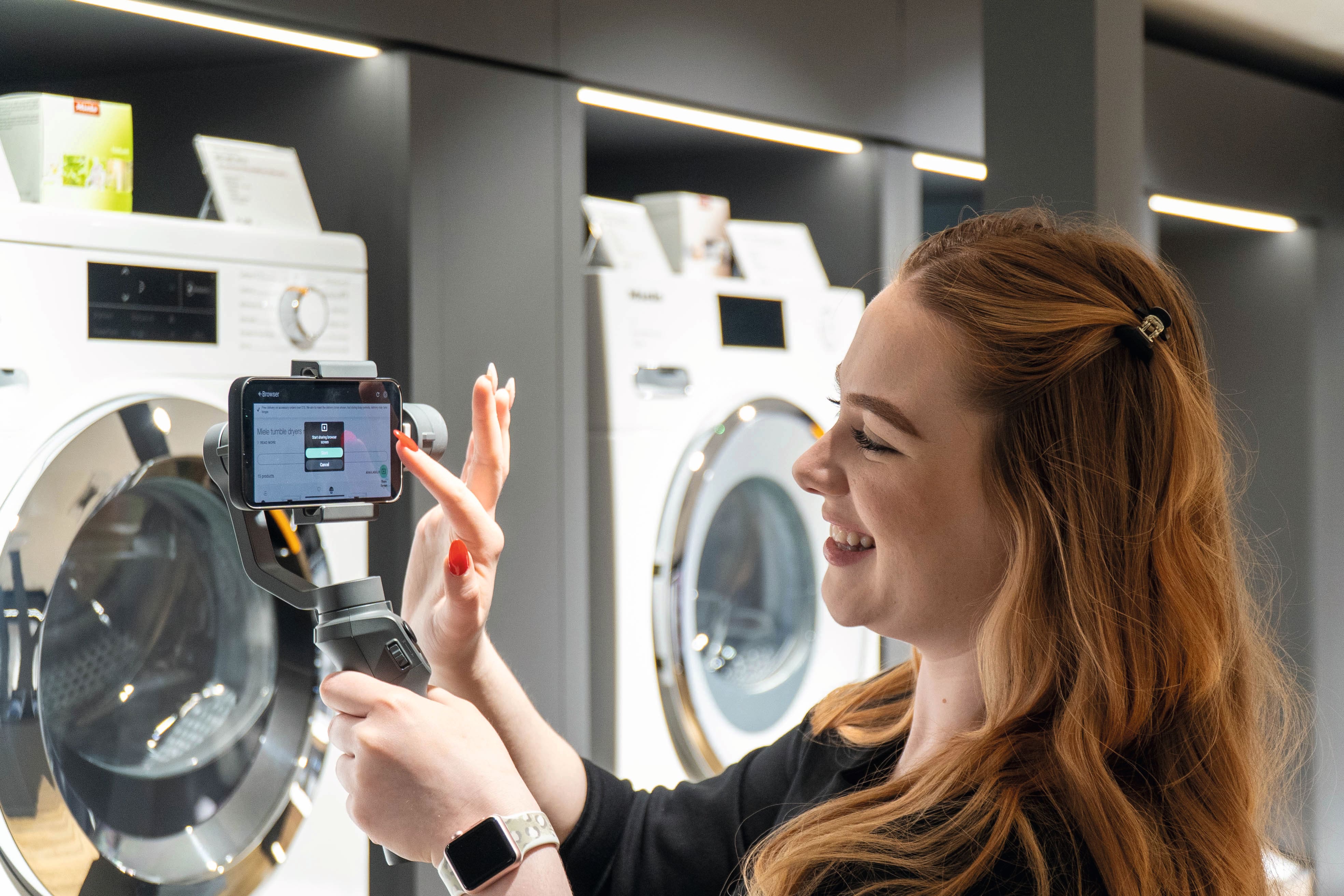 Une personne enregistre une démonstration de produit avec un smartphone sur un stabilisateur dans un showroom d'appareils électroménagers, à côté de machines à laver et sèche-linge modernes. Une personne enregistre une démonstration de produit avec un smartphone sur un stabilisateur dans un showroom d'appareils électroménagers, à côté de machines à laver et sèche-linge modernes.