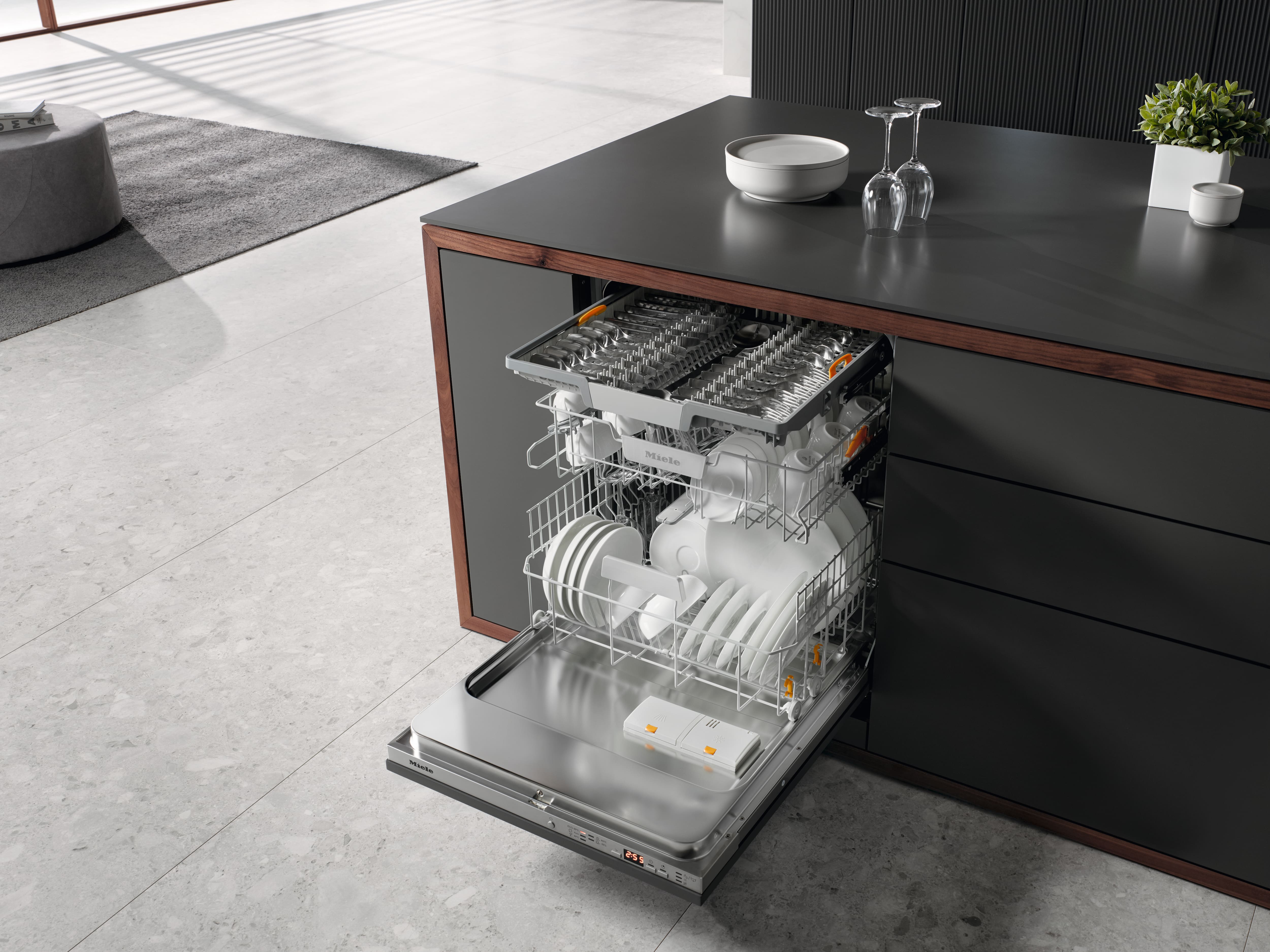 Open Miele built-in dishwasher in a modern kitchen island, fully loaded with dishes and cutlery, ready for a wash cycle. Open Miele built-in dishwasher in a modern kitchen island, fully loaded with dishes and cutlery, ready for a wash cycle.