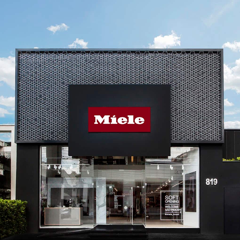 Fachada da loja Miele no Brasil com padrão geométrico e entrada de vidro, destacando o logo e o número 819. Fachada da loja Miele no Brasil com padrão geométrico e entrada de vidro, destacando o logo e o número 819.
