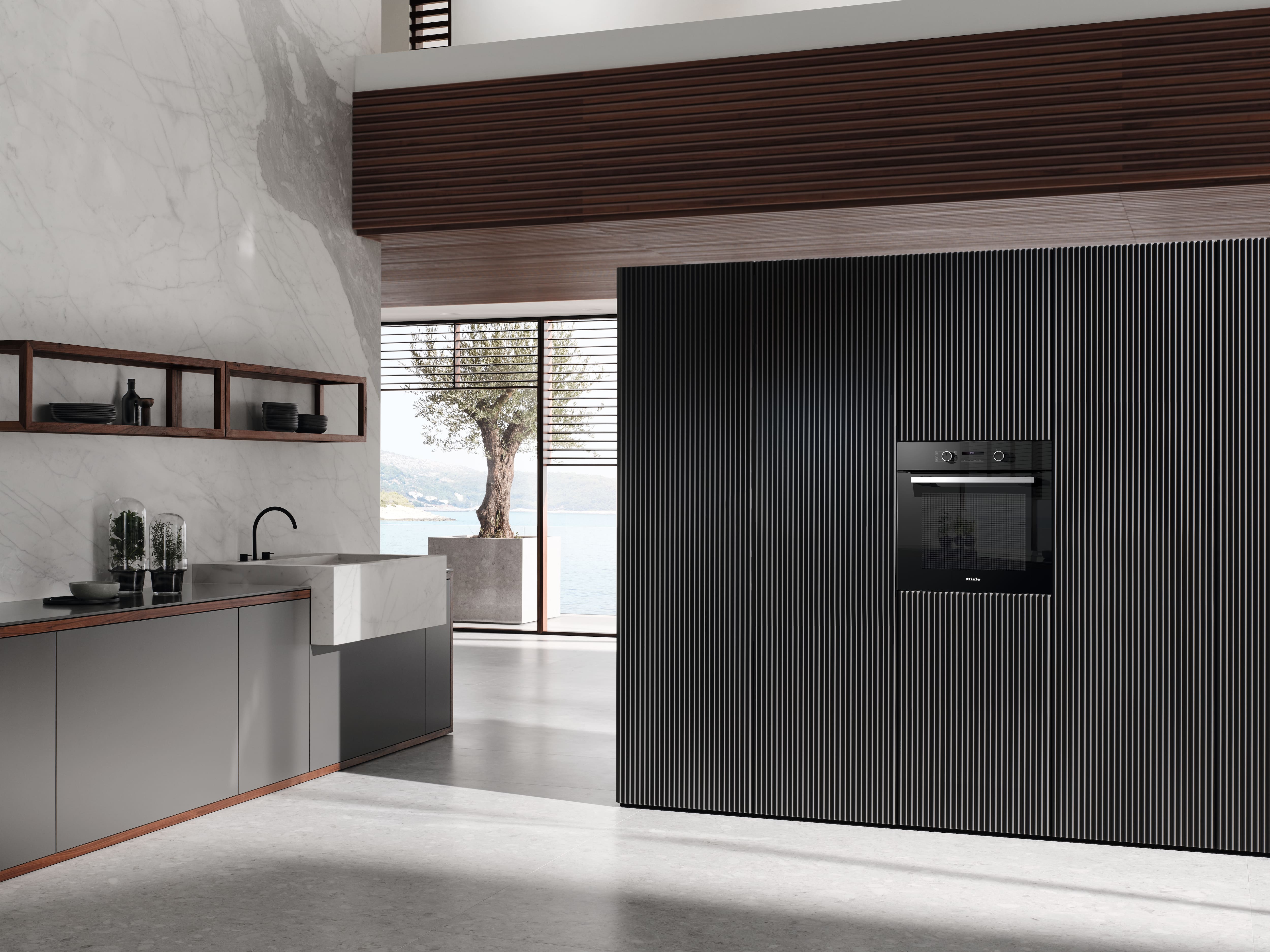 Black Miele kitchen appliances in a dark kitchen with an open steam oven and vegetables in it