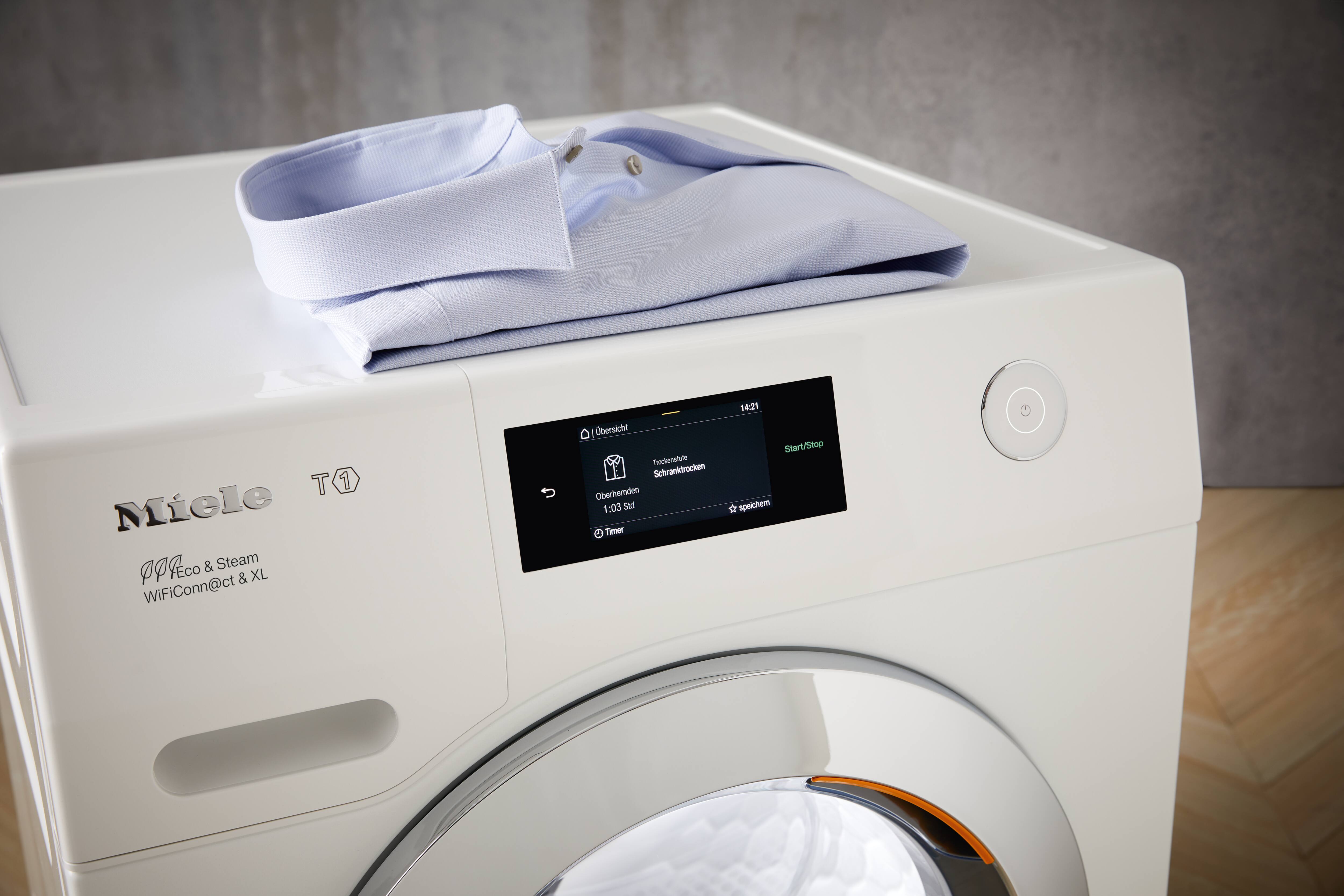 Close-up de uma secadora Miele T1 Eco & Steam de 9 kg com tela sensível ao toque, com uma camisa social azul-clara dobrada apoiada sobre ela. Close-up de uma secadora Miele T1 Eco & Steam de 9 kg com tela sensível ao toque, com uma camisa social azul-clara dobrada apoiada sobre ela.