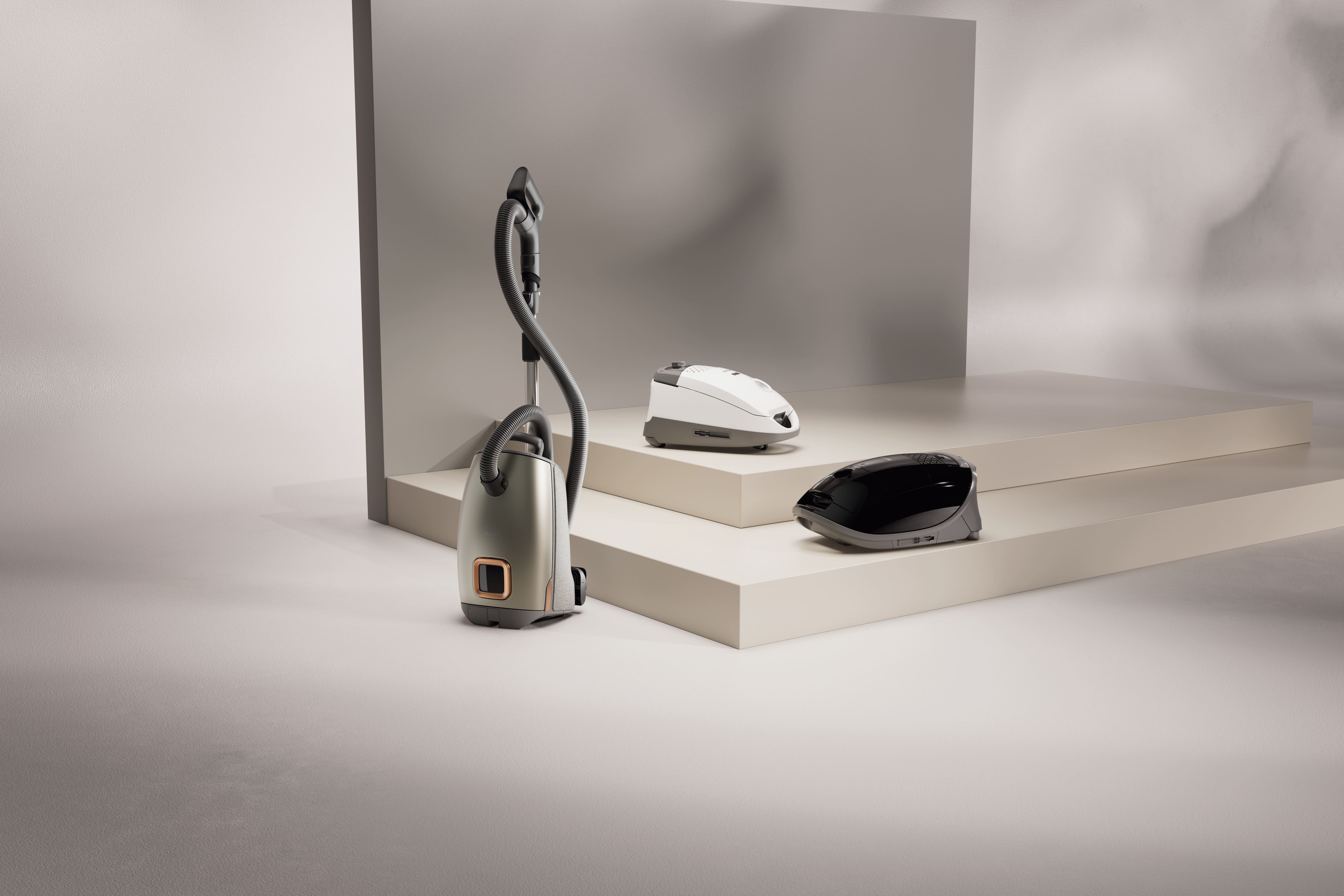 Three modern Miele Guard vacuum cleaners in a minimalist studio Three modern Miele Guard vacuum cleaners in a minimalist studio