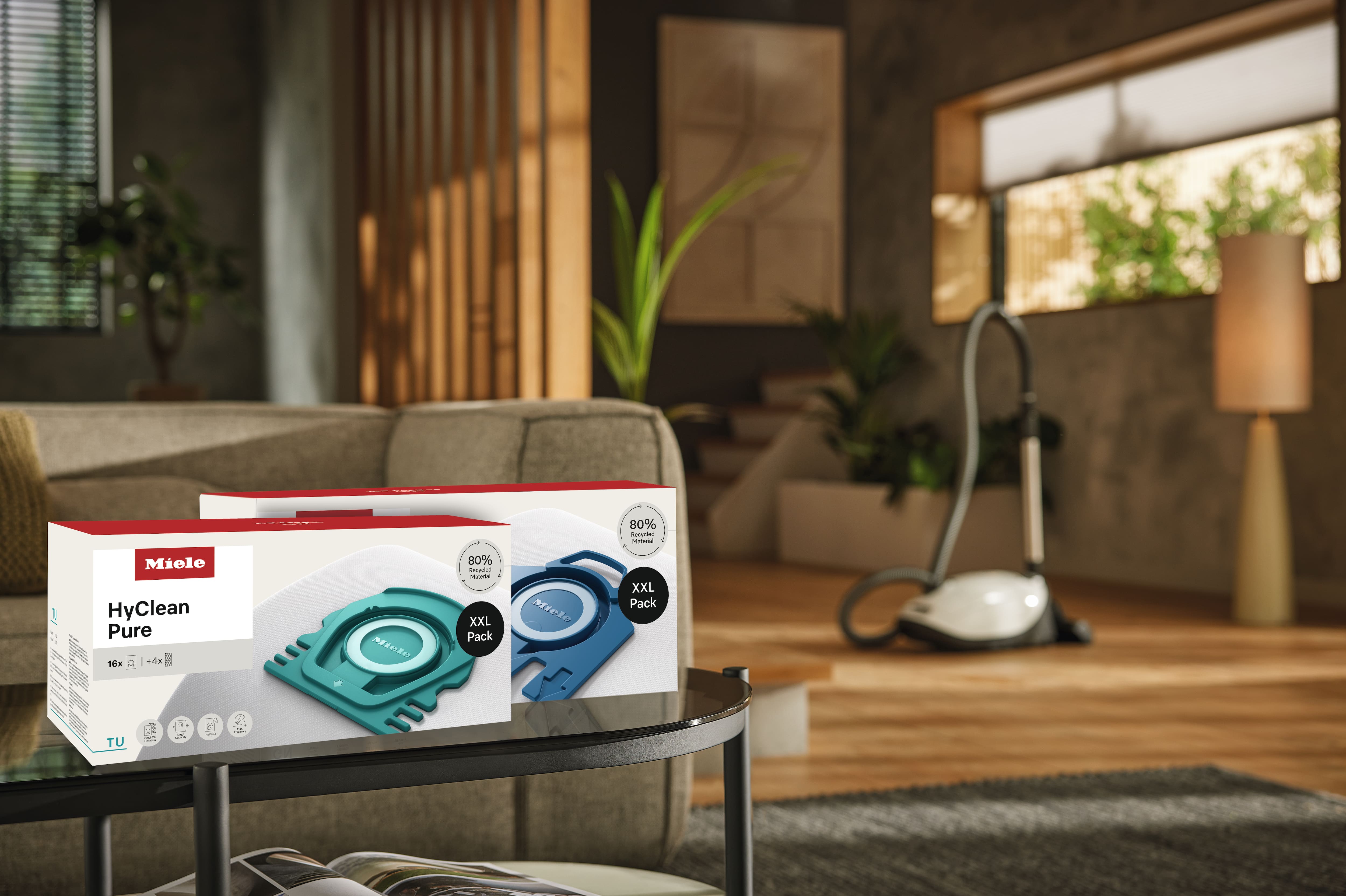 Doos met Miele HyClean Pure stofzuigerzakken op salontafel in gezellige woonkamer; sledestofzuiger op de achtergrond. Doos met Miele HyClean Pure stofzuigerzakken op salontafel in gezellige woonkamer; sledestofzuiger op de achtergrond.