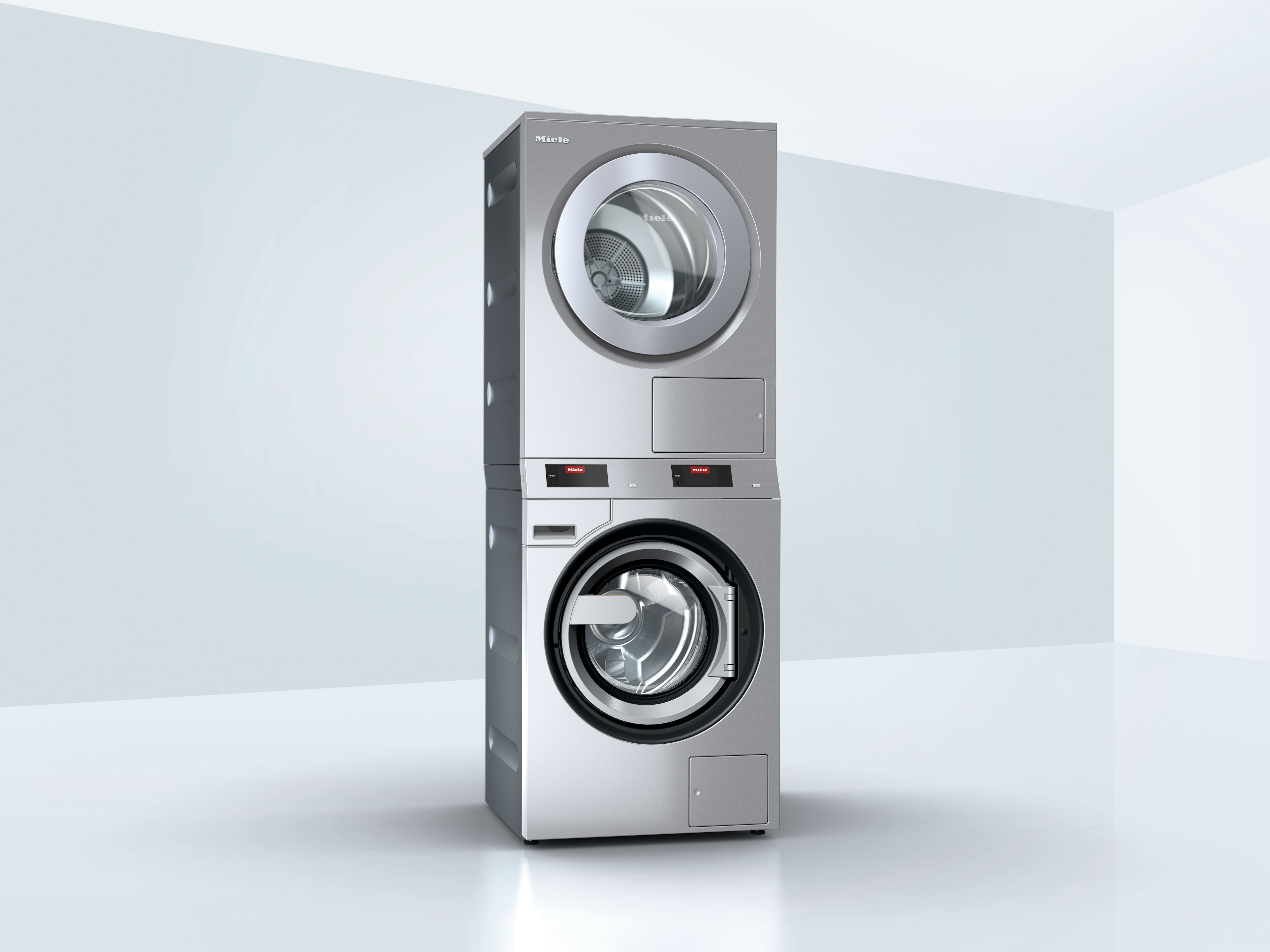 Stacked stainless steel front‑loading washer and dryer unit in a minimal light gray room, with visible Miele branding on the control panels.