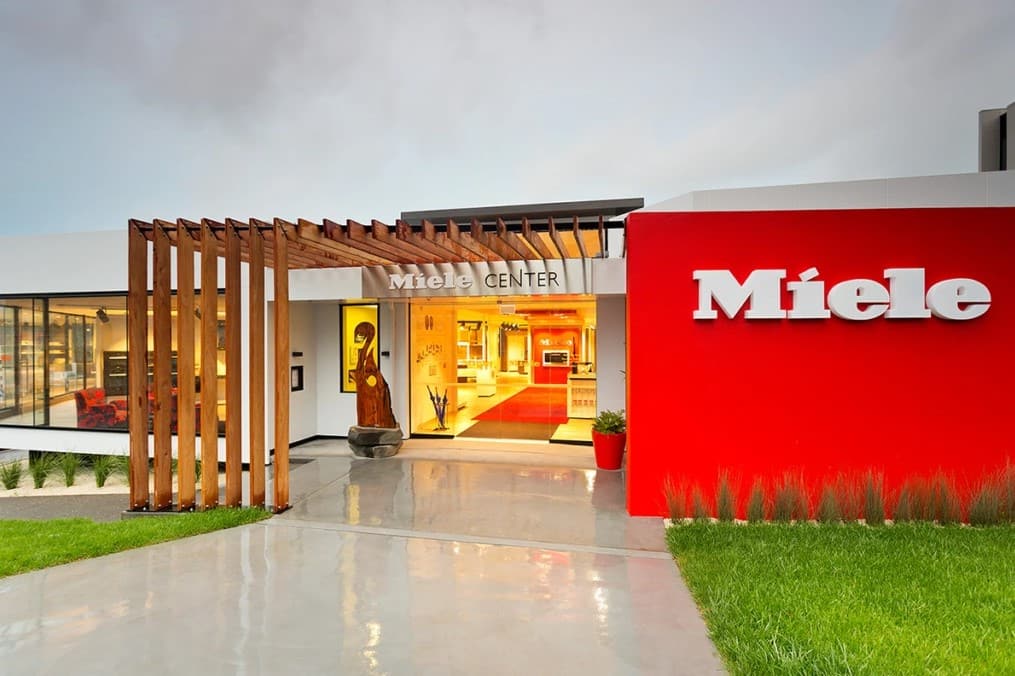 Modern Miele Center showroom entrance in Auckland with red feature wall, wood pergola, and glossy wet walkway.