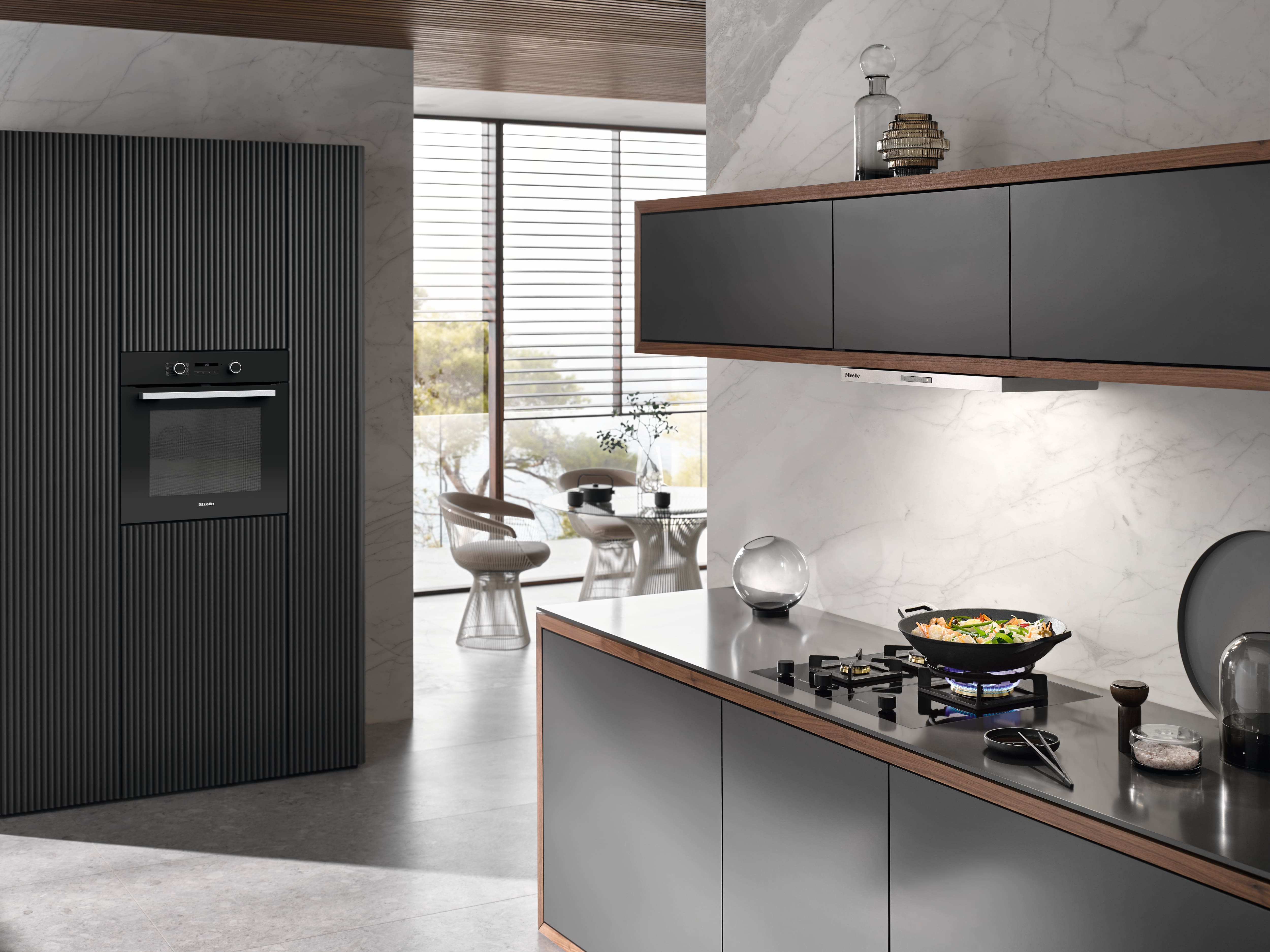 Modern kitchen with brass island featuring modular gas, teppanyaki, and induction cooktop; dining set nearby. Modern kitchen with brass island featuring modular gas, teppanyaki, and induction cooktop; dining set nearby.