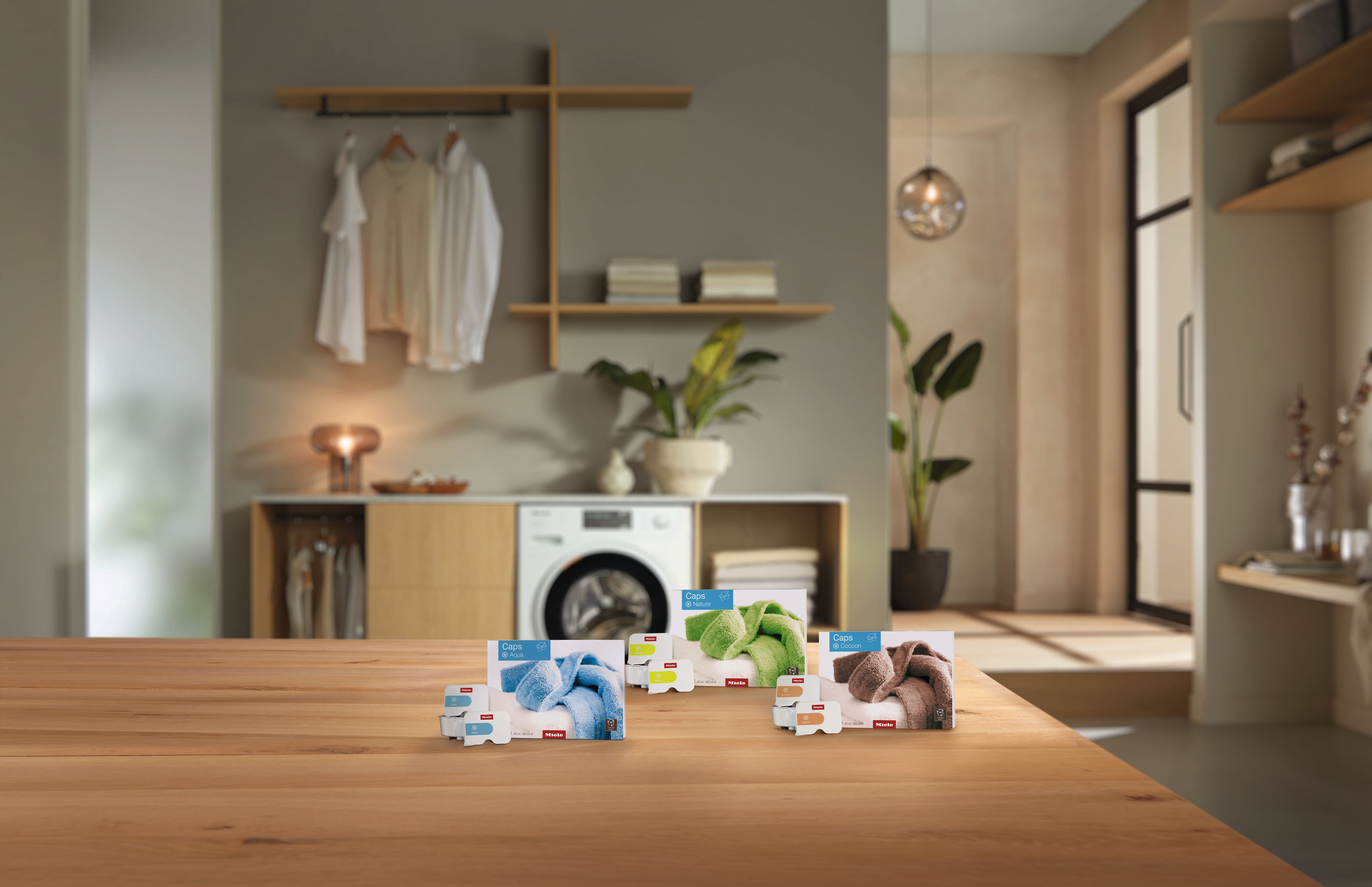 Stylish laundry room with washer; Miele Caps detergent and fabric care packs displayed on a wooden countertop.