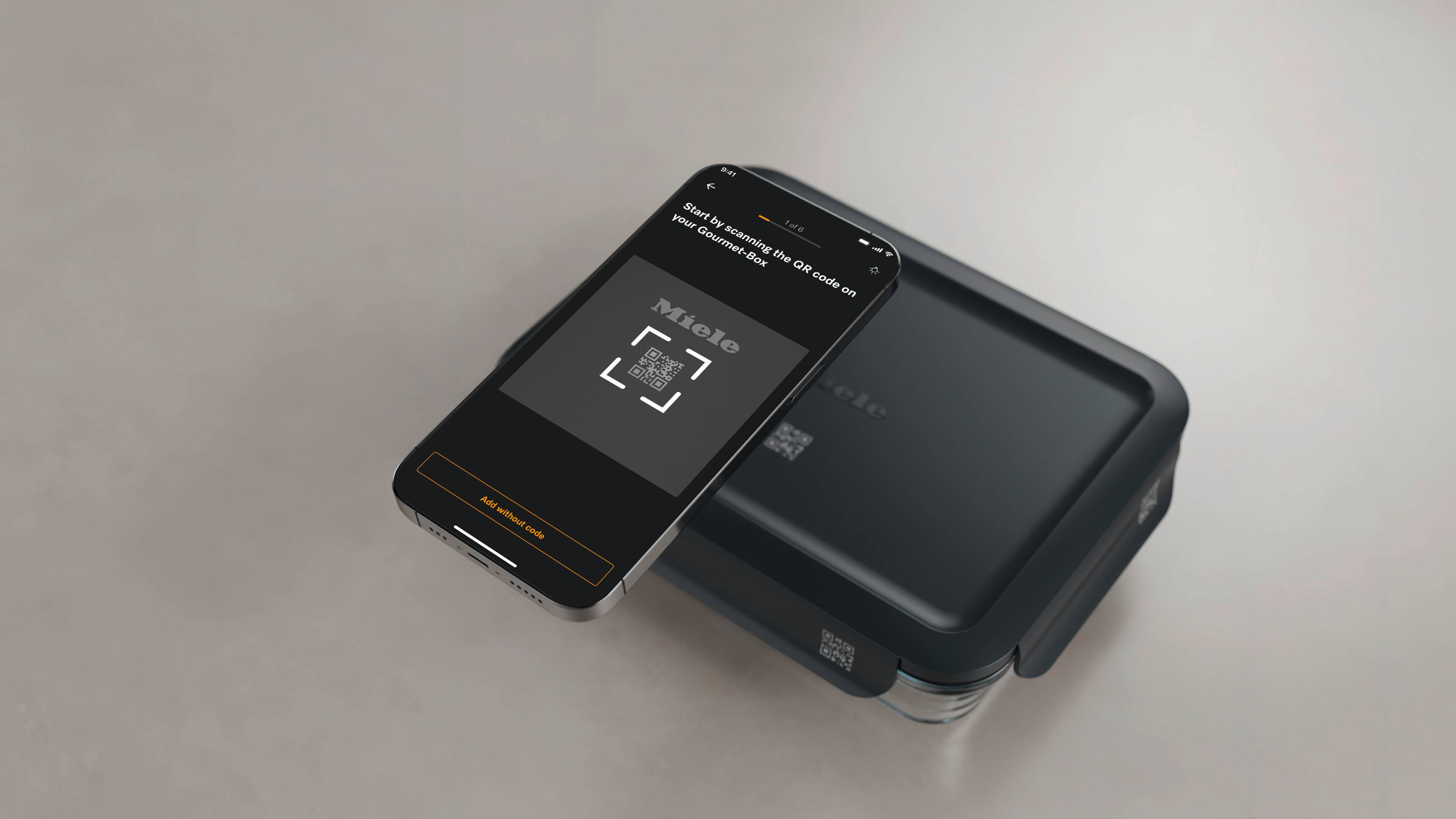 Smartphone scanning a QR code with an app to register a Miele container, showing a storage box with QR label on a table. Smartphone scanning a QR code with an app to register a Miele container, showing a storage box with QR label on a table.