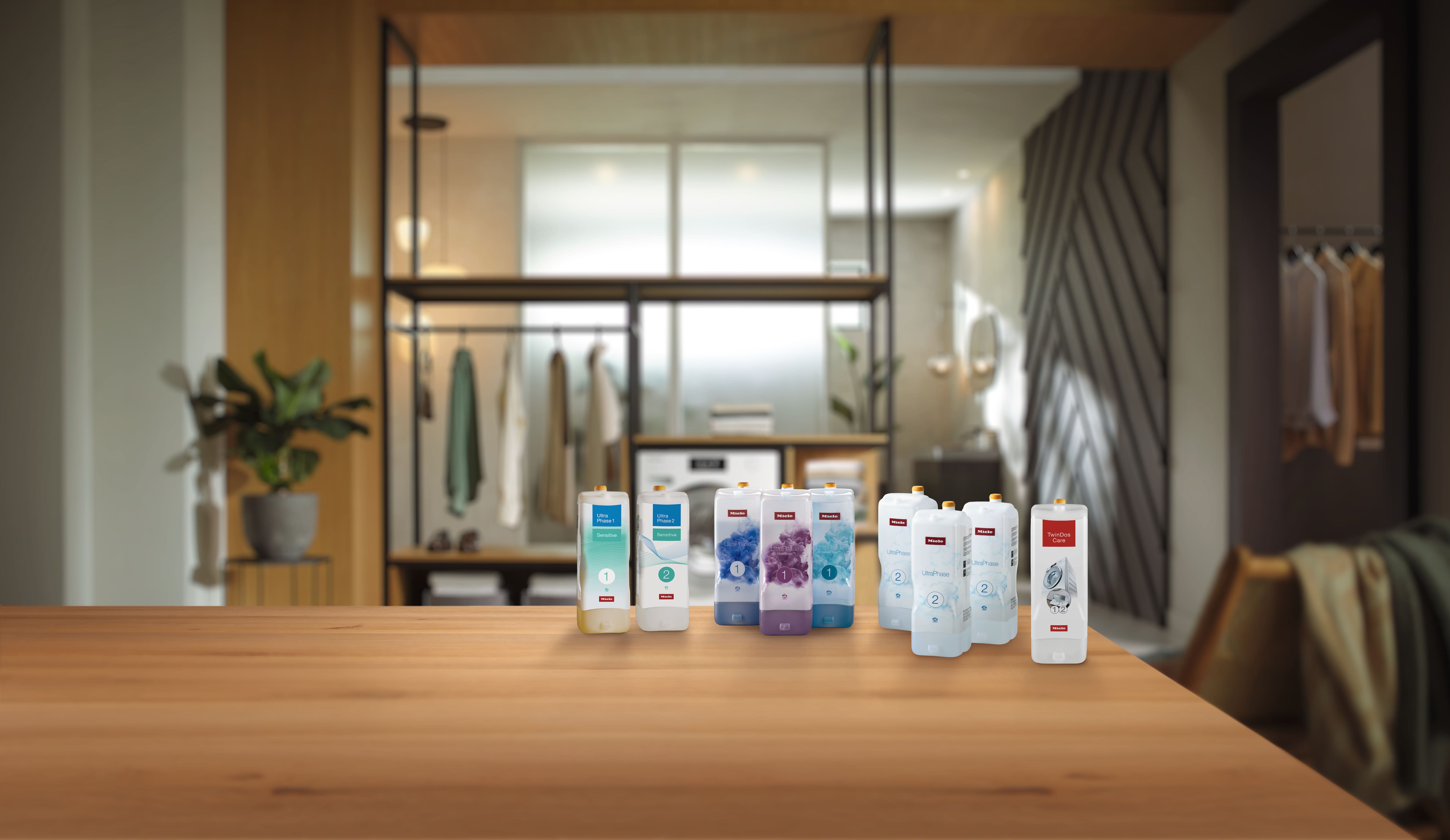 Assorted laundry detergent and care cartridges arranged on a wooden countertop in a modern closet-laundry room.