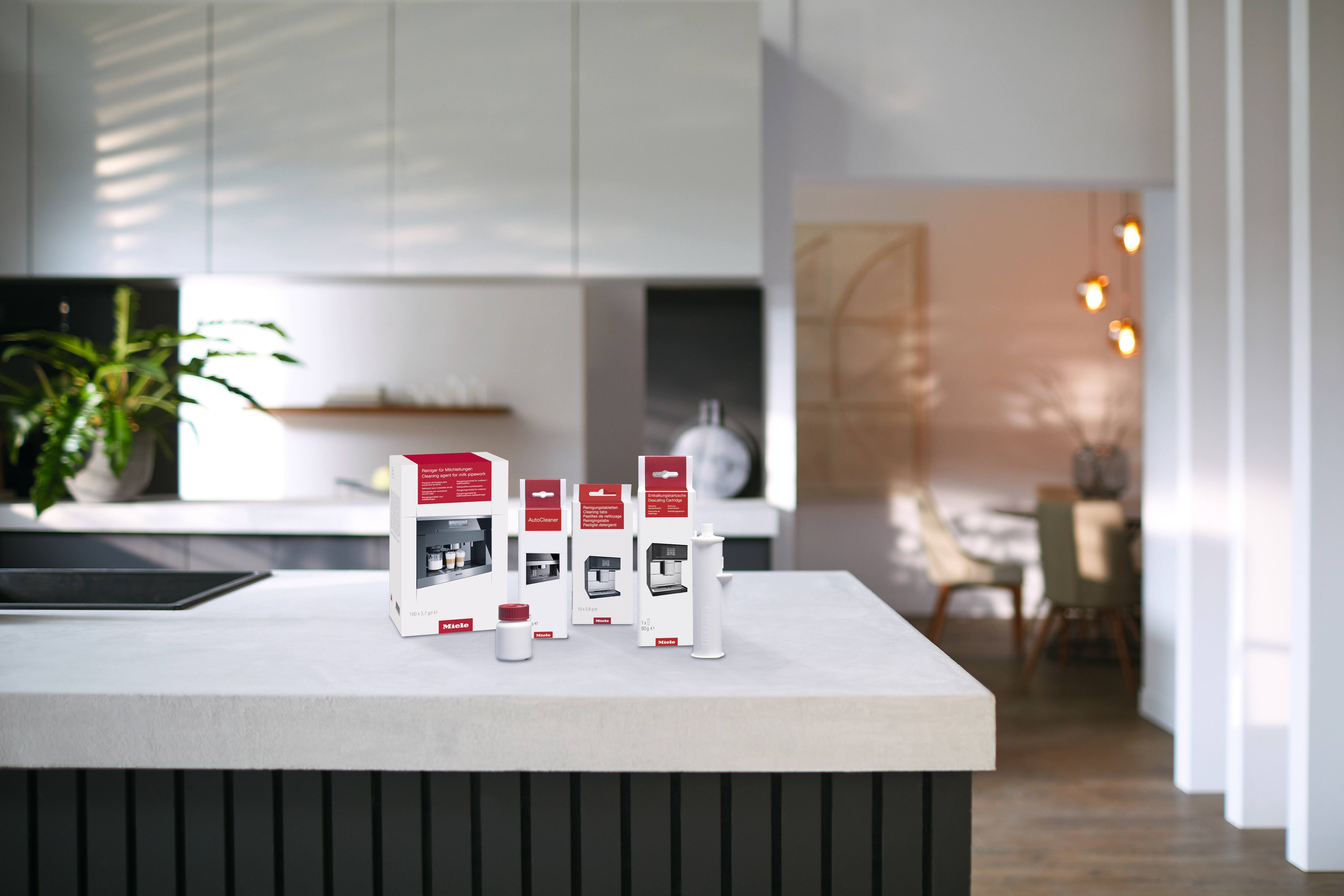 Bancada de cozinha moderna com kits de limpeza e descalcificação para a máquina de café Miele, além de um frasco e uma ferramenta para a manutenção do eletrodoméstico. Bancada de cozinha moderna com kits de limpeza e descalcificação para a máquina de café Miele, além de um frasco e uma ferramenta para a manutenção do eletrodoméstico.