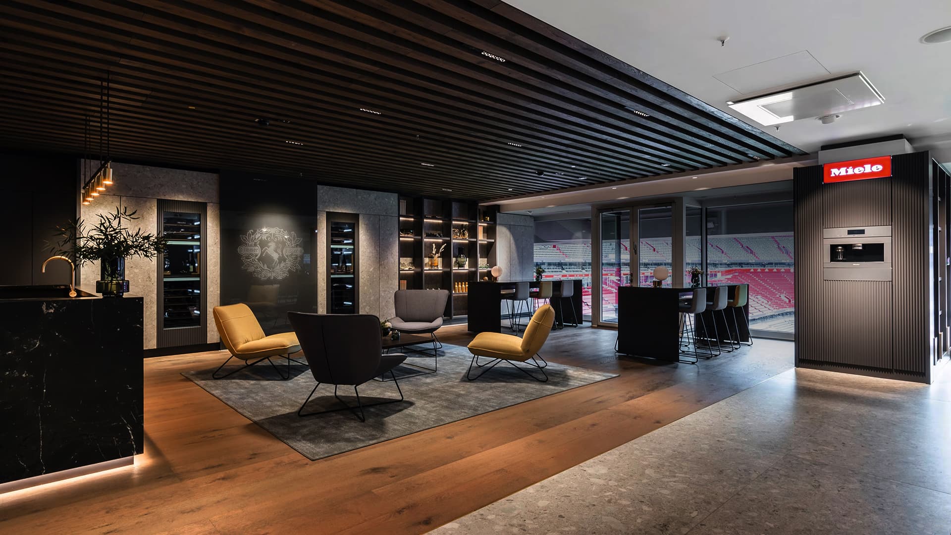 Moderne Stadion-Lounge mit gemütlichen Sitzbereichen, Holzlamellendecke und stilvollen Barzonen. Elegante Miele Geräte fügen sich harmonisch in das hochwertige Ambiente ein. Moderne Stadion-Lounge mit gemütlichen Sitzbereichen, Holzlamellendecke und stilvollen Barzonen. Elegante Miele Geräte fügen sich harmonisch in das hochwertige Ambiente ein.