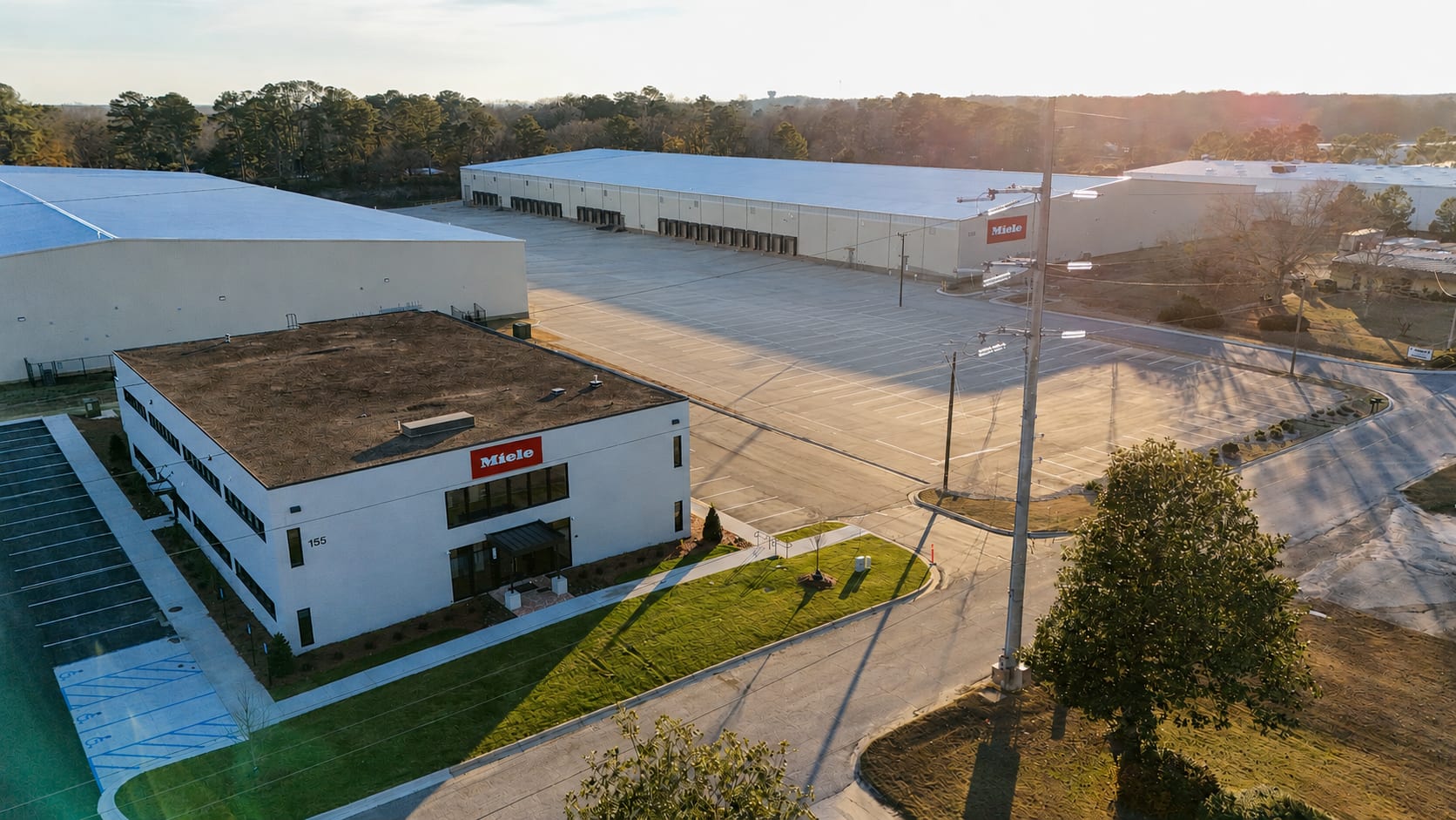 Aerial view of a Miele distribution complex featuring an office building, large warehouses, loading docks, and empty parking areas.