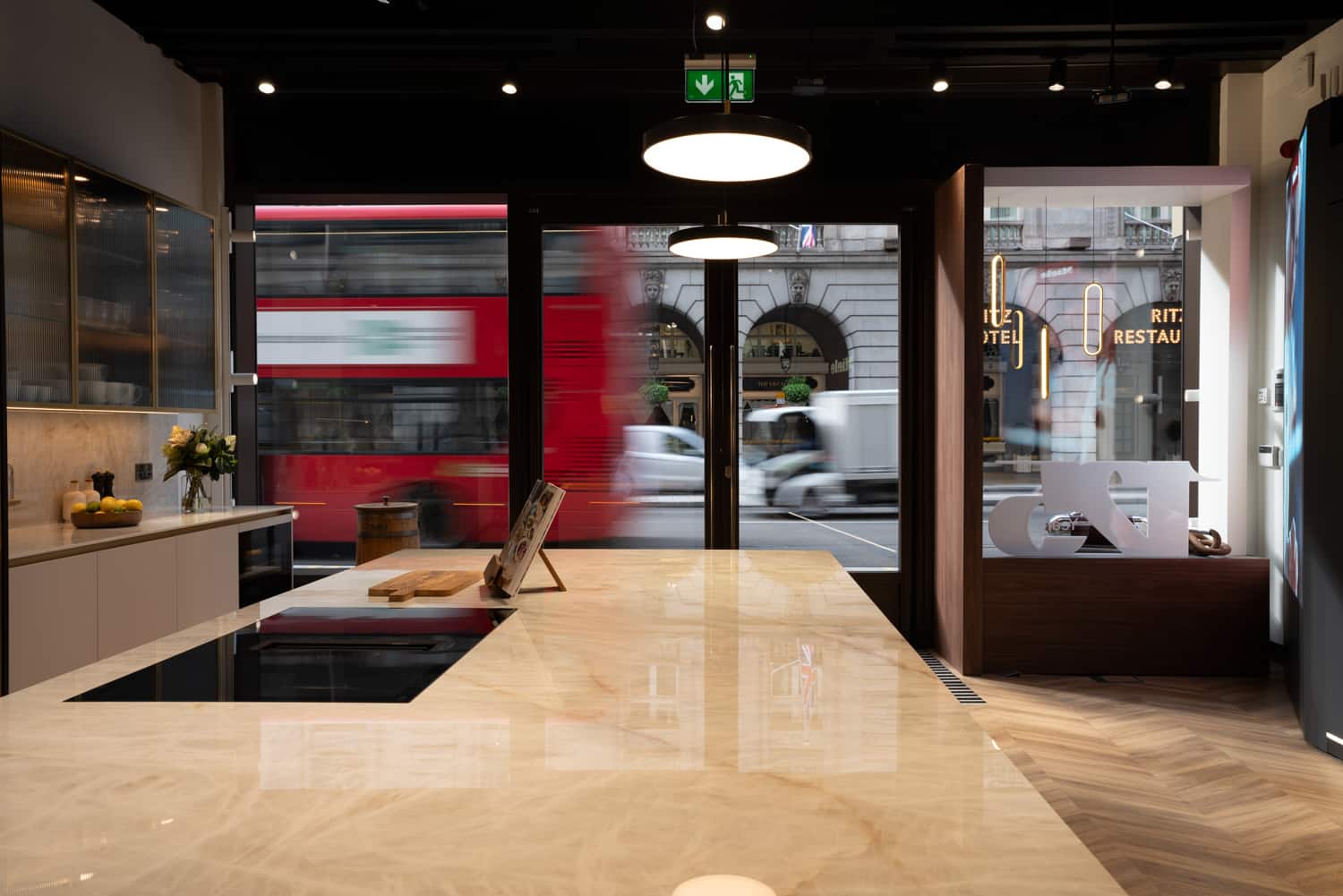 Modern kitchen showroom with marble island and pendant lights, looking out to a London street with a passing red bus. Modern kitchen showroom with marble island and pendant lights, looking out to a London street with a passing red bus.
