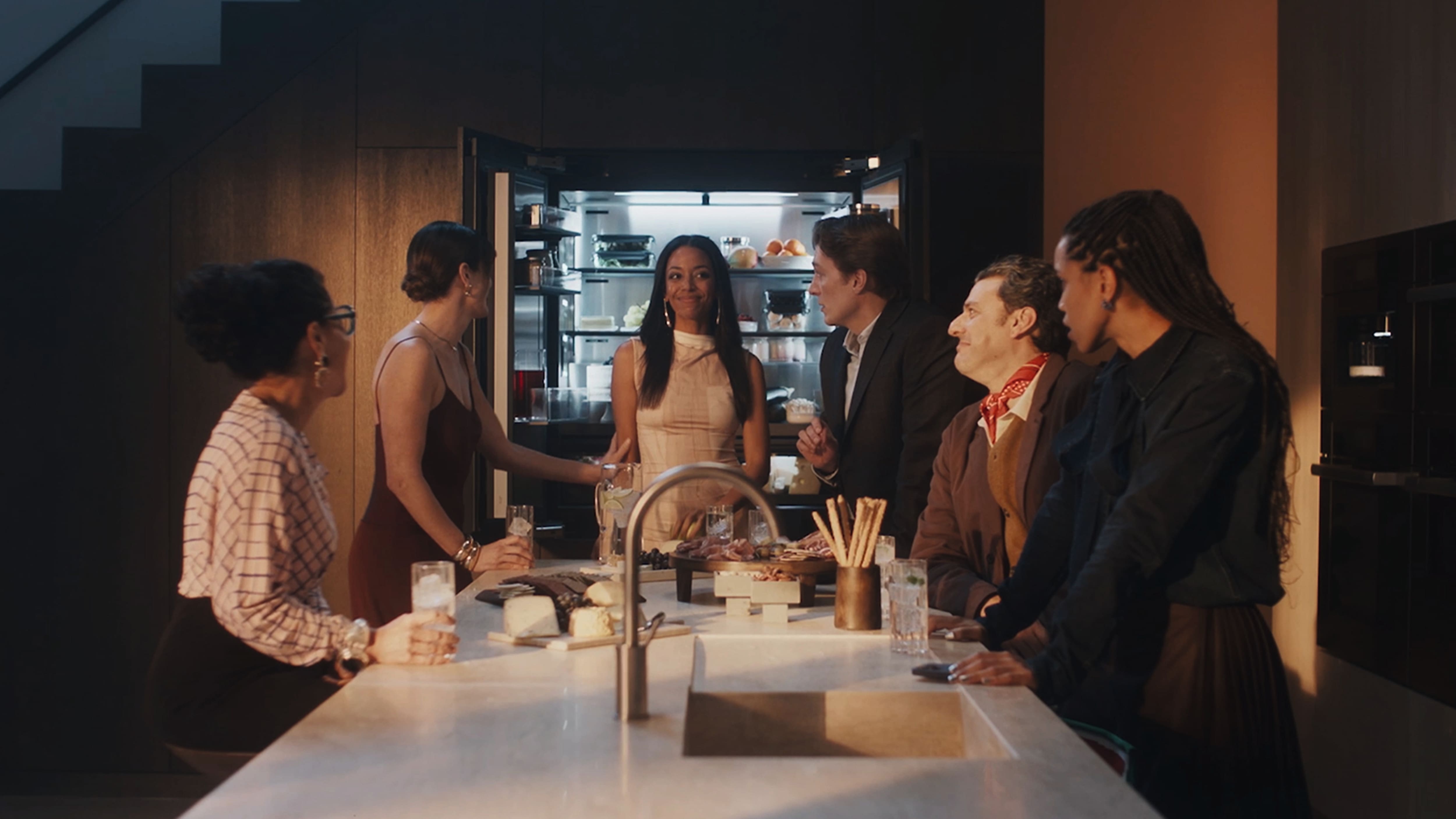 Friends gather in a modern kitchen, chatting around a marble island with drinks and snacks; open fridge glowing behind. Friends gather in a modern kitchen, chatting around a marble island with drinks and snacks; open fridge glowing behind.