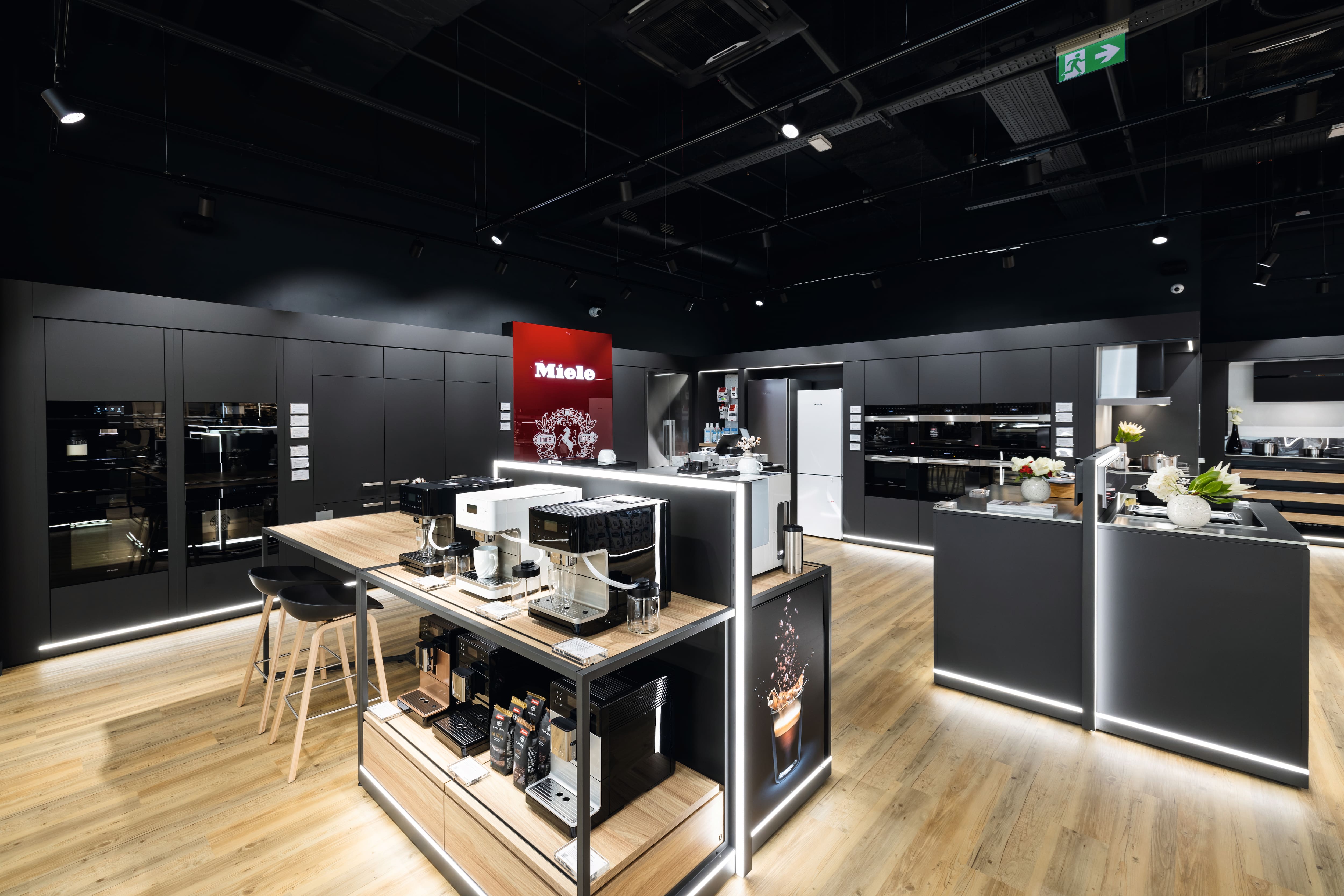 Mūsdienīgs sadzīves tehnikas salons ar Miele zīmolu, kurā izstādītas kafijas automāti, iebūvētās krāsnis un eleganti tumši skapji. Mūsdienīgs sadzīves tehnikas salons ar Miele zīmolu, kurā izstādītas kafijas automāti, iebūvētās krāsnis un eleganti tumši skapji.