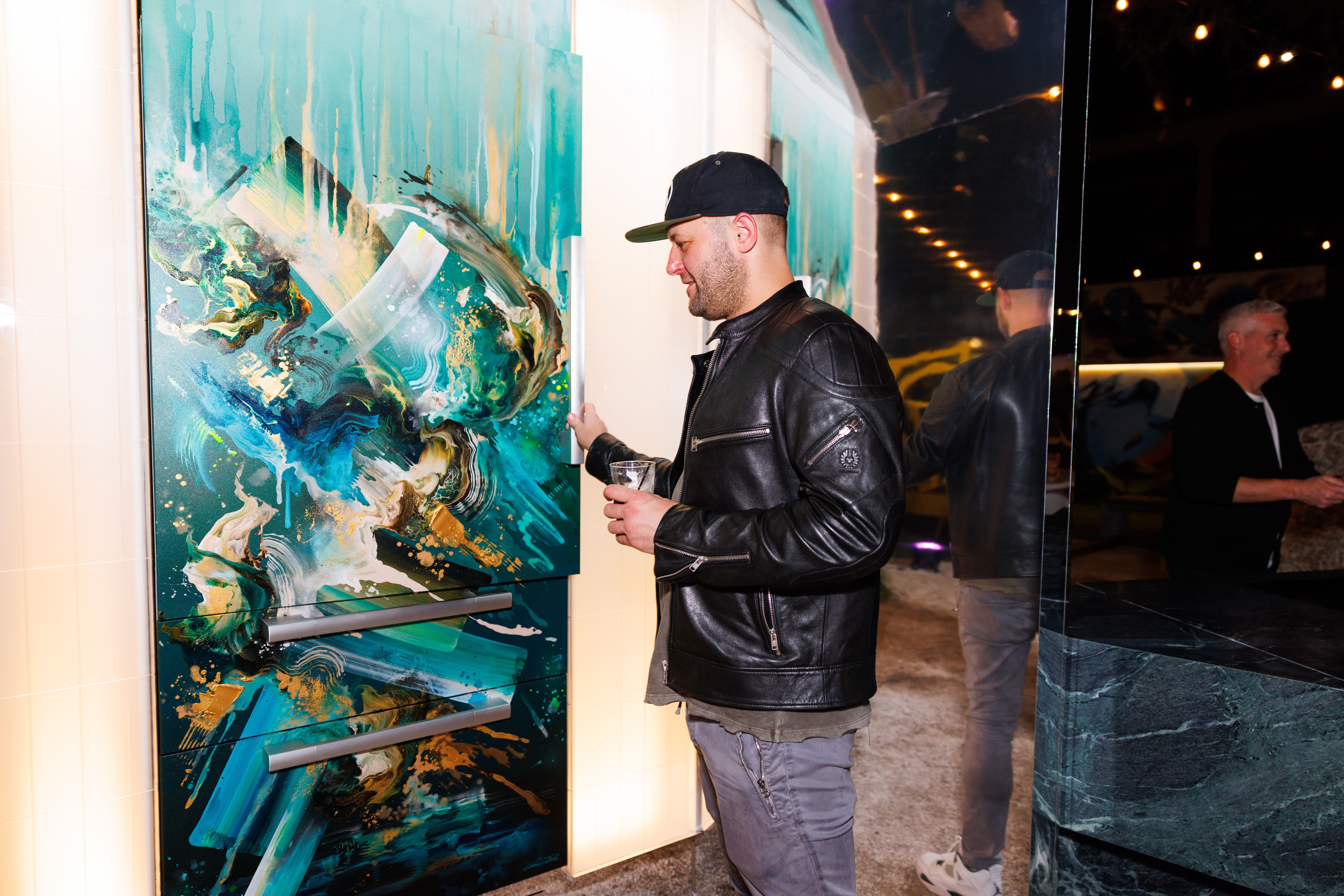 Artist interacts with a custom Miele appliance clad in colorful abstract artwork, showcasing the fusion of contemporary art, premium design, and kitchen innovation at The Kitchen Muse. Artist interacts with a custom Miele appliance clad in colorful abstract artwork, showcasing the fusion of contemporary art, premium design, and kitchen innovation at The Kitchen Muse.