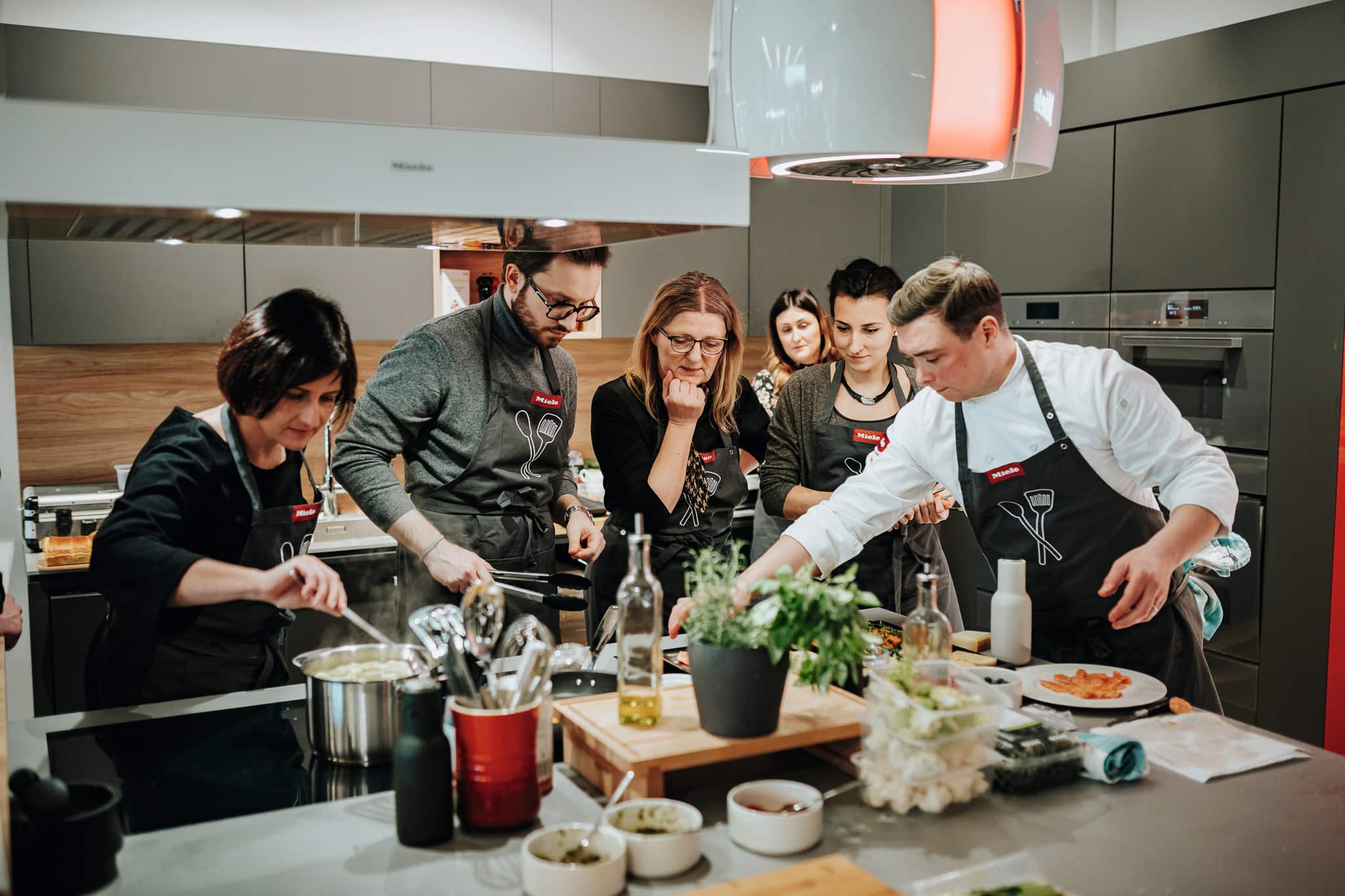 Group cooking class in a modern kitchen, instructor guiding participants as they prepare dishes at a counter. Group cooking class in a modern kitchen, instructor guiding participants as they prepare dishes at a counter.