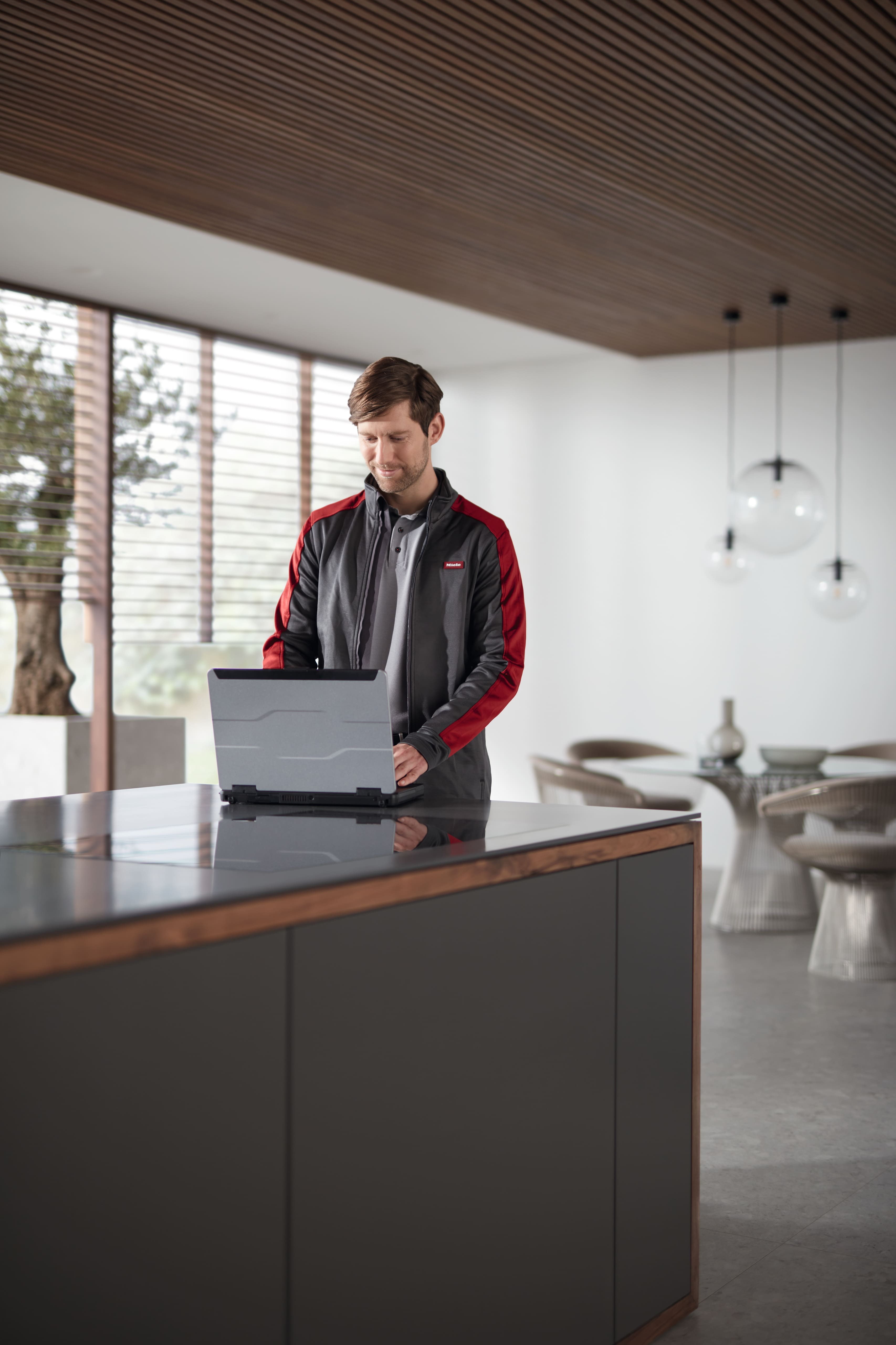 Une personne utilise un ordinateur portable sur un îlot de cuisine épuré, dans un intérieur moderne et lumineux.