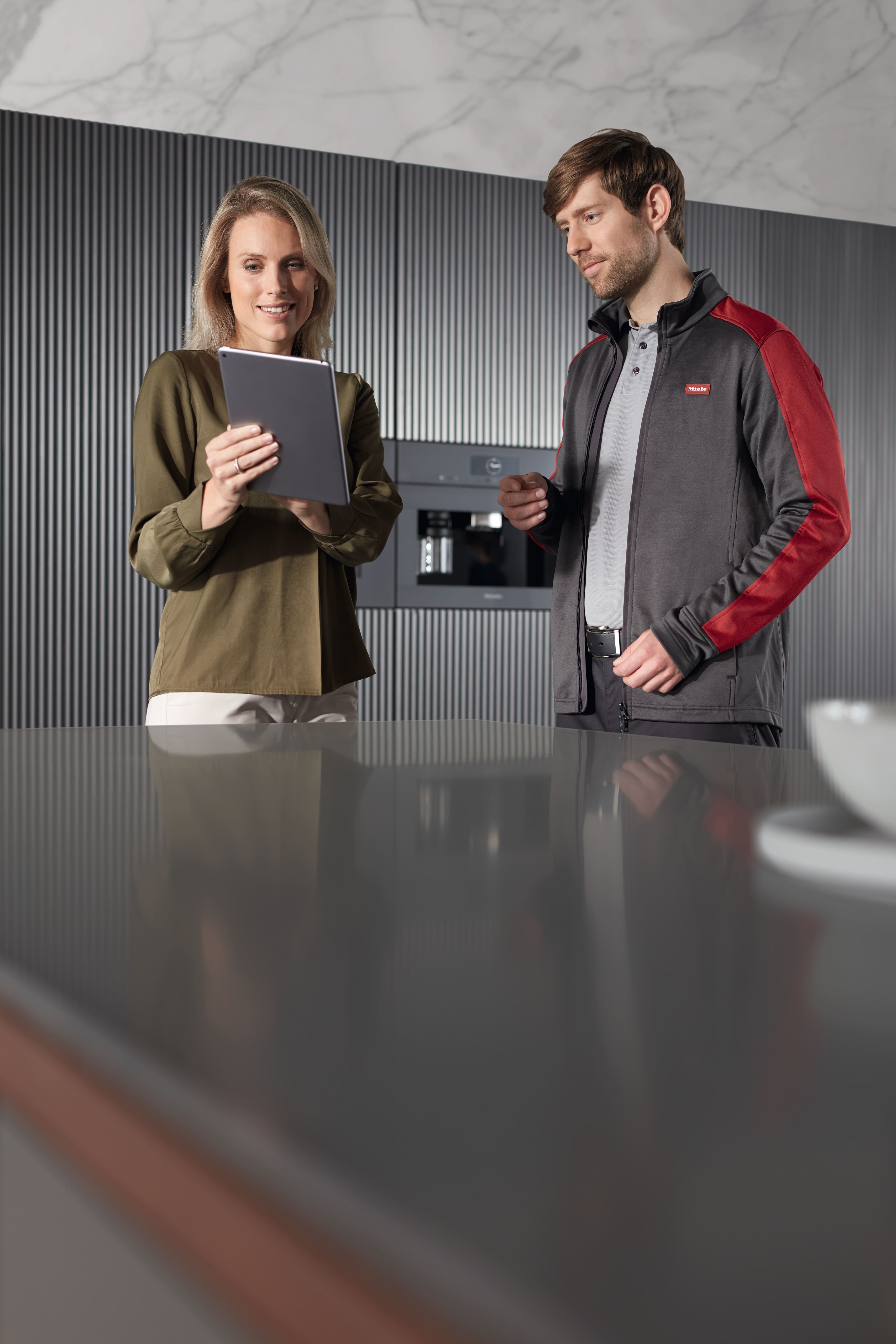 Technician and homeowner review details on a tablet in a modern kitchen with built-in coffee machine.