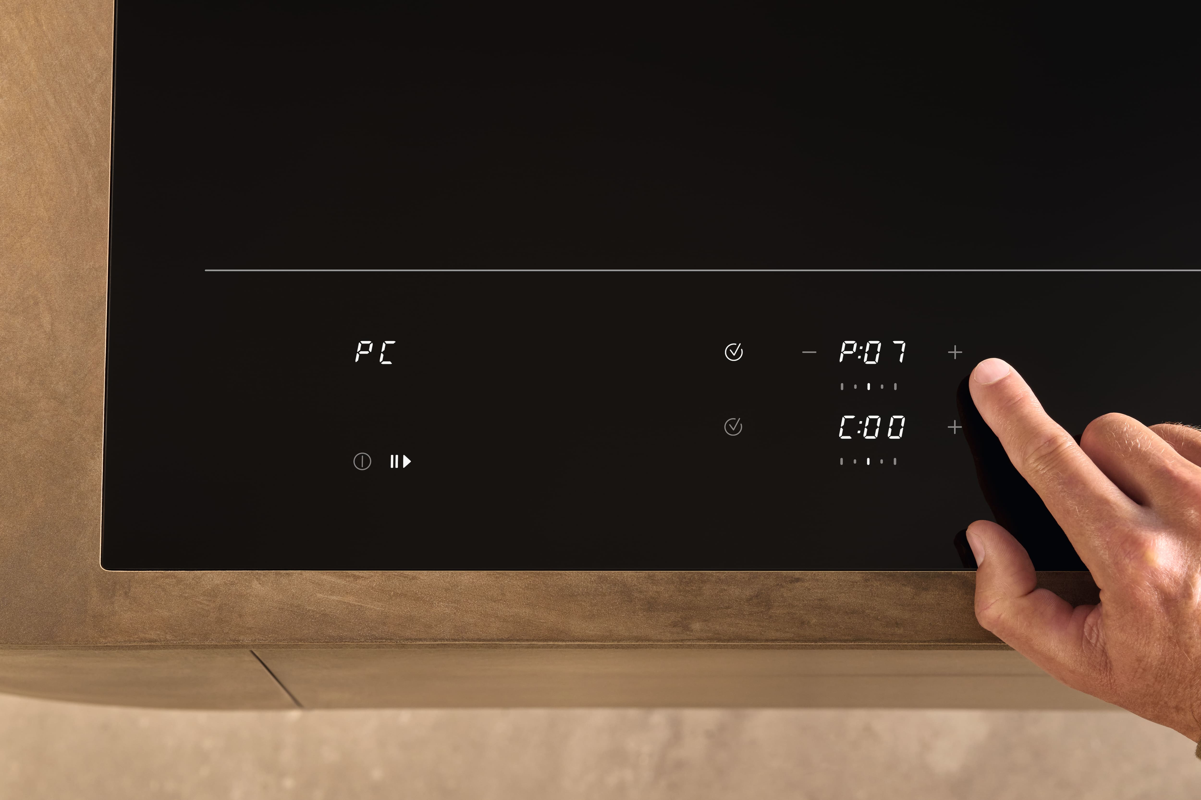 Close-up of an induction cooktop’s touch controls; a hand taps plus to raise power, with display showing P:07. Close-up of an induction cooktop’s touch controls; a hand taps plus to raise power, with display showing P:07.