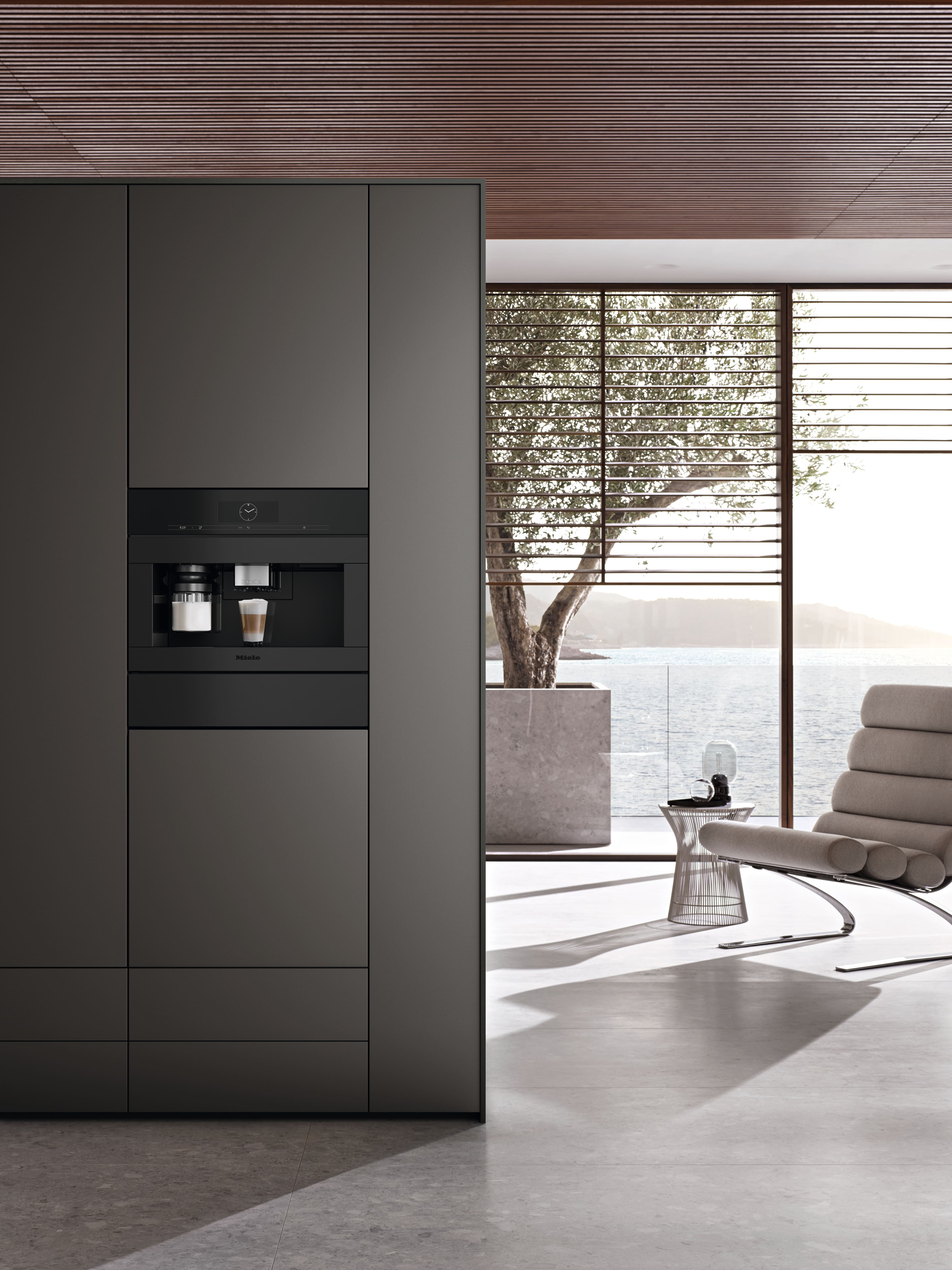 Modern kitchen with built-in espresso machine beside a minimalist lounge, large windows, and waterfront view. Modern kitchen with built-in espresso machine beside a minimalist lounge, large windows, and waterfront view.