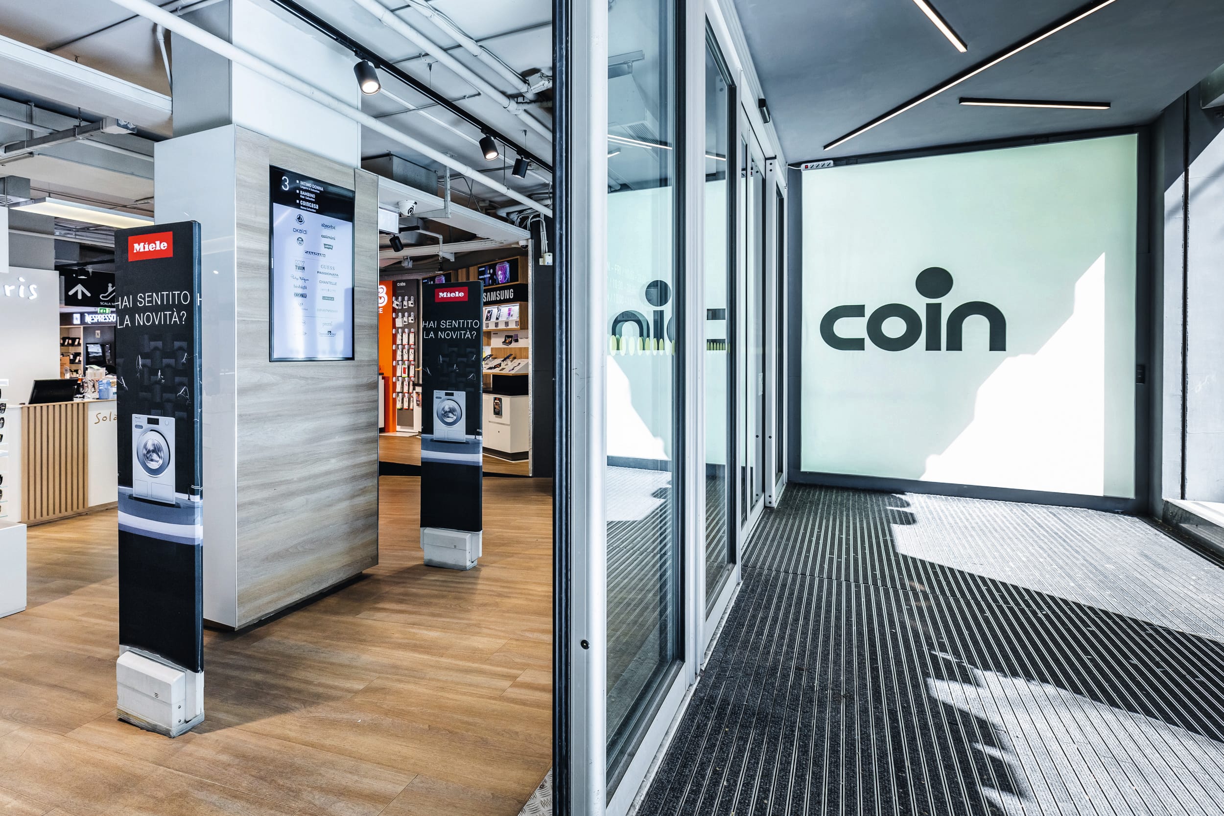 Ingresso moderno di un grande magazzino con porte scorrevoli in vetro, grande logo “coin”, pavimenti in legno e esposizioni di elettronica/elettrodomestici. Ingresso moderno di un grande magazzino con porte scorrevoli in vetro, grande logo “coin”, pavimenti in legno e esposizioni di elettronica/elettrodomestici.