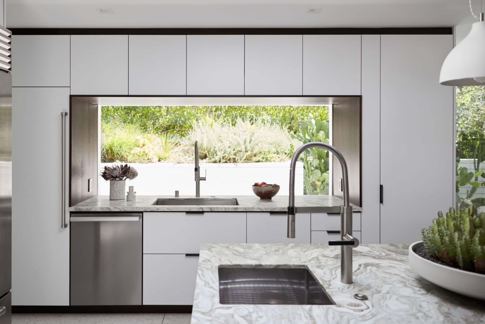 Minimalist kitchen with marble island and sink, large window to garden, sleek white cabinetry and steel fixtures. Minimalist kitchen with marble island and sink, large window to garden, sleek white cabinetry and steel fixtures.