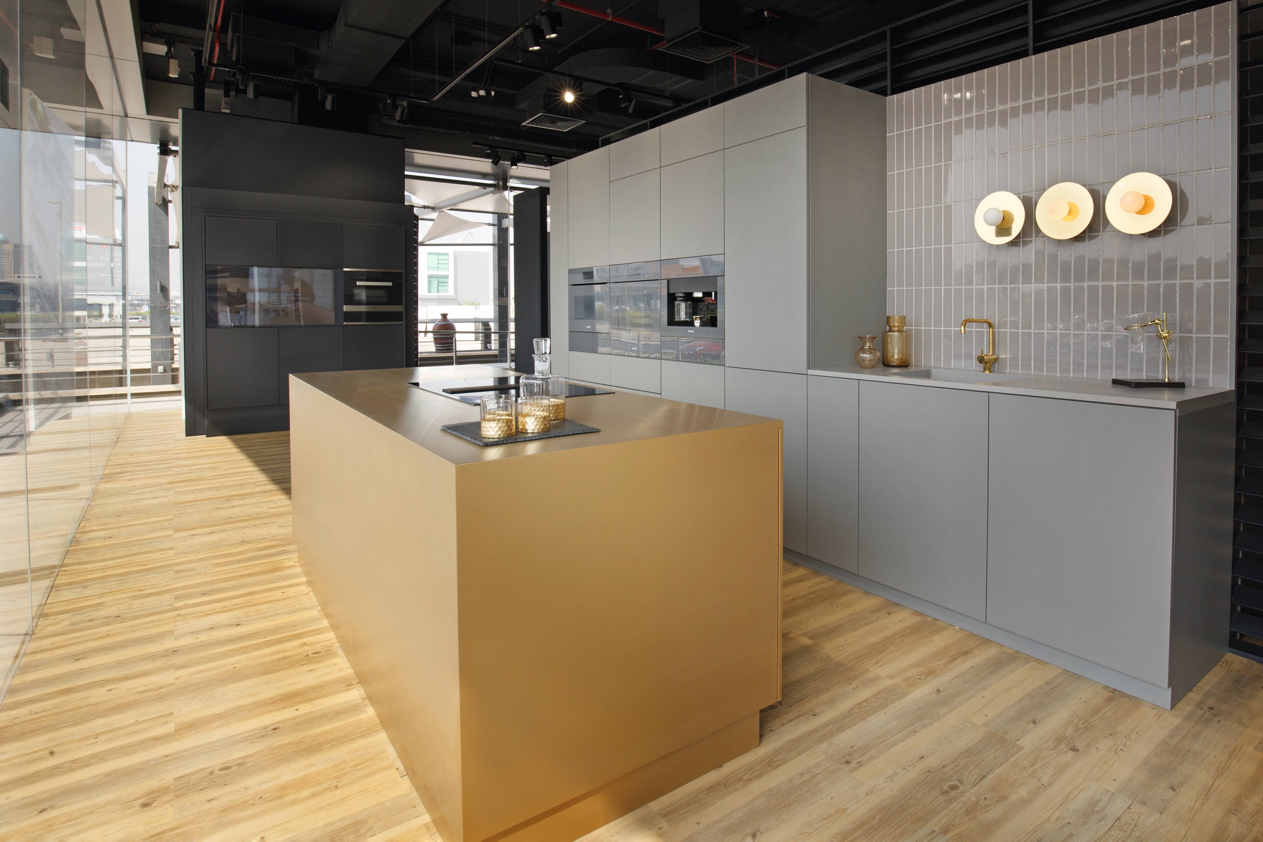 Modern showroom kitchen with gold island, gray cabinets, brass fixtures, and built-in appliances. Modern showroom kitchen with gold island, gray cabinets, brass fixtures, and built-in appliances.
