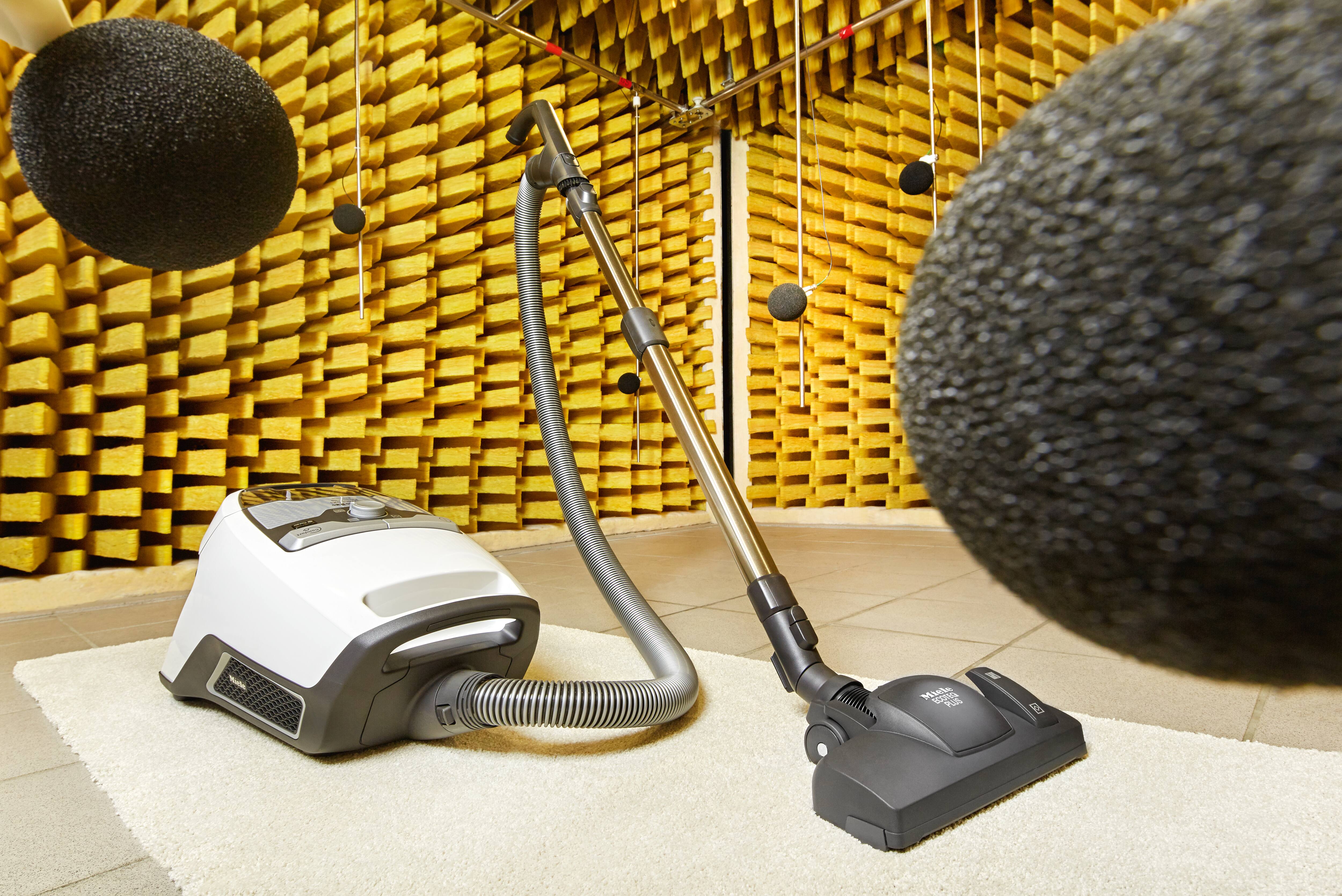 Canister vacuum on a white rug inside an anechoic chamber, surrounded by suspended microphones for noise testing. Canister vacuum on a white rug inside an anechoic chamber, surrounded by suspended microphones for noise testing.