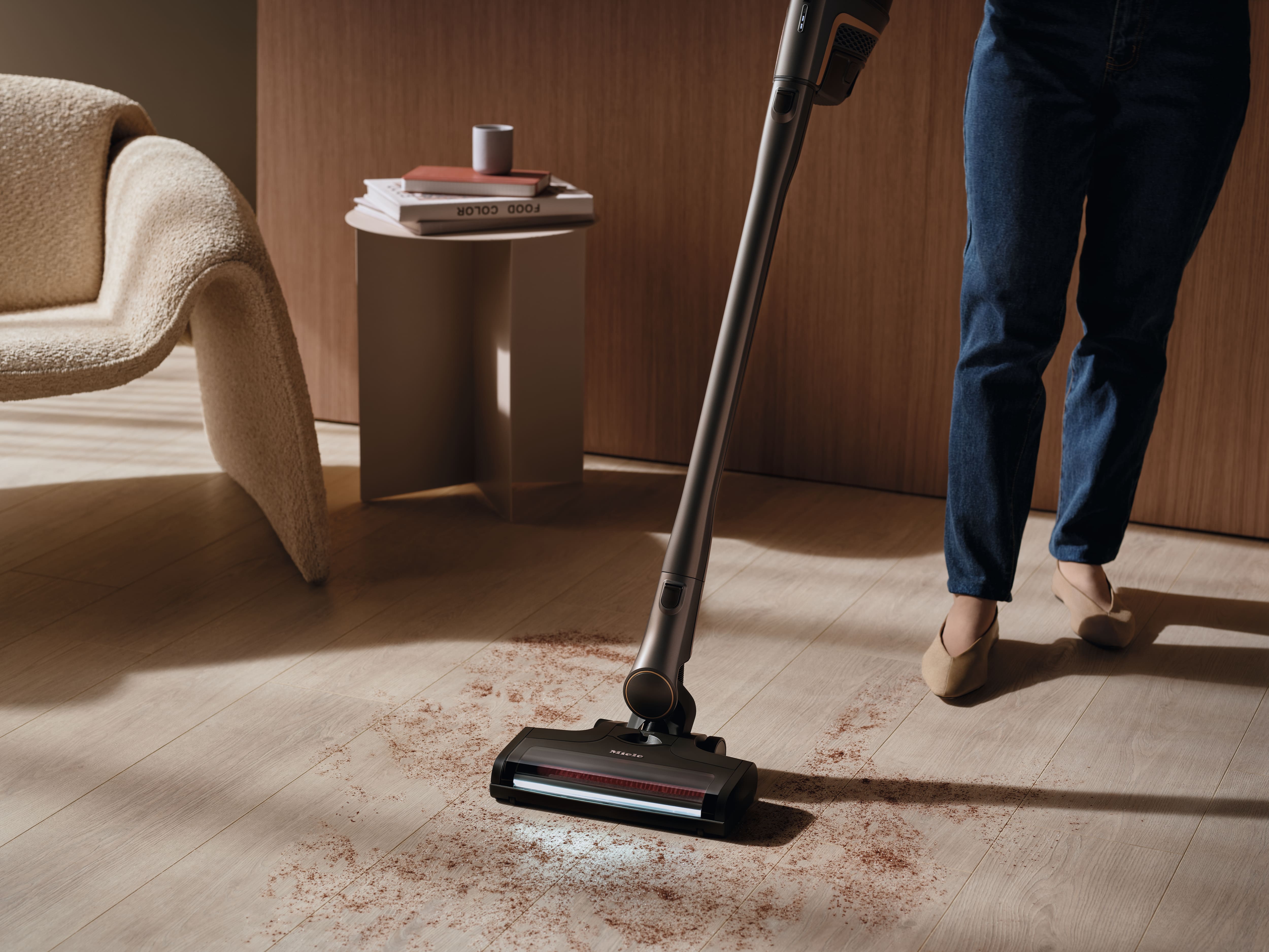 Personne utilisant un aspirateur balai sans fil pour nettoyer la saleté sur un sol en bois clair dans un salon moderne. Personne utilisant un aspirateur balai sans fil pour nettoyer la saleté sur un sol en bois clair dans un salon moderne.