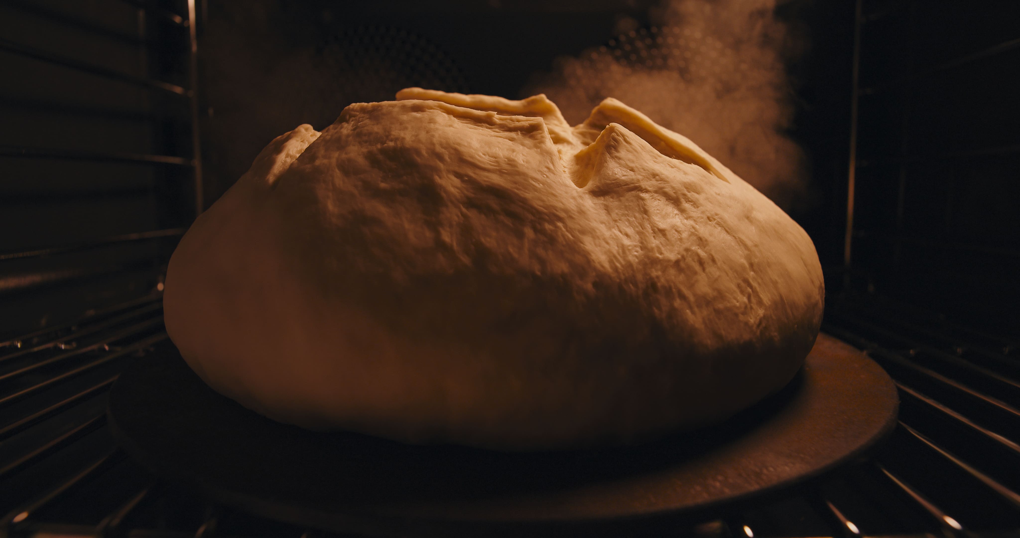 Close-up of a round loaf of bread baking on a stone in a hot oven, dough rising with steam. Close-up of a round loaf of bread baking on a stone in a hot oven, dough rising with steam.
