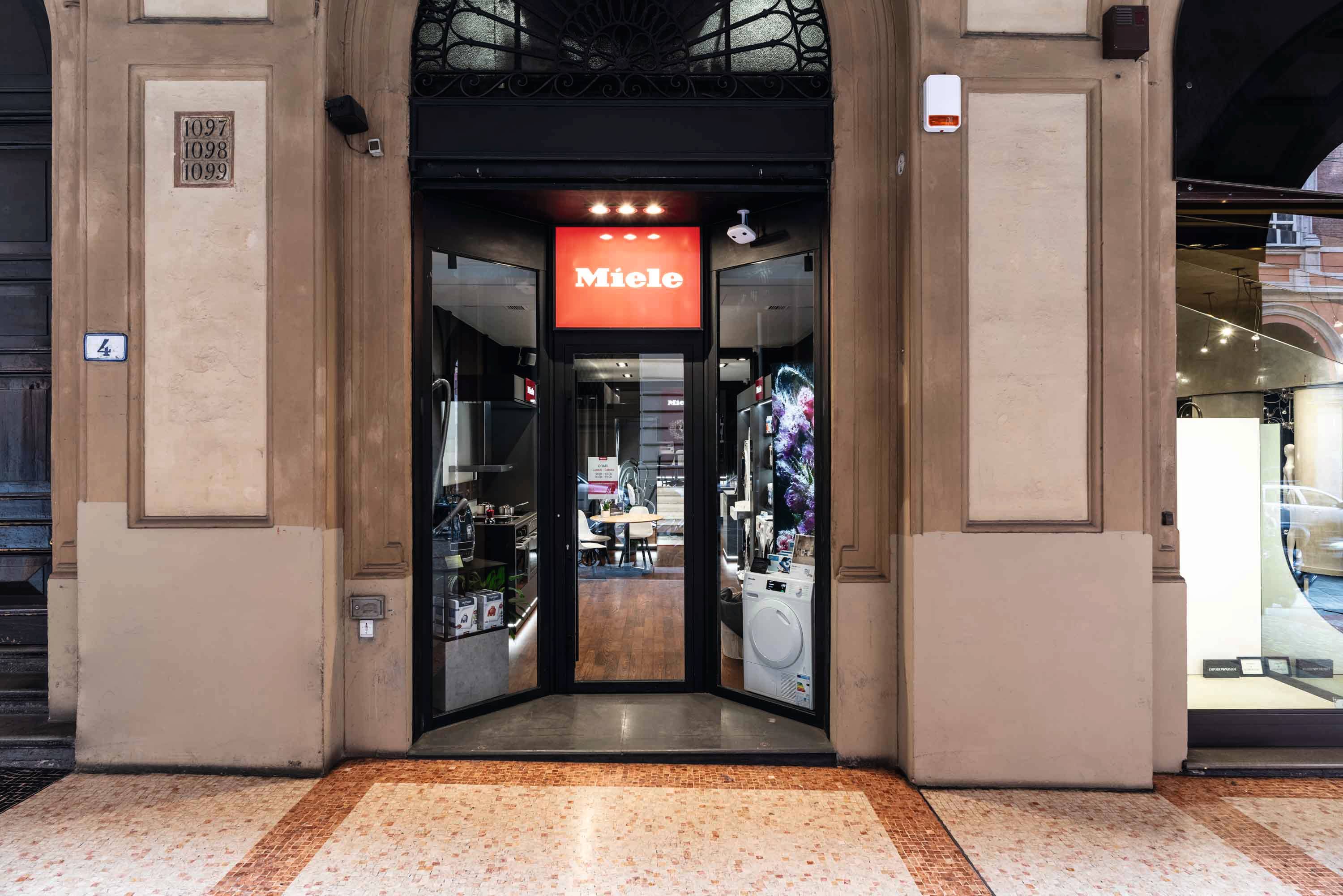 Vetrina a livello strada con facciata ad arco; insegna Miele sopra l'ingresso in vetro che rivela uno showroom di elettrodomestici all'interno. Vetrina a livello strada con facciata ad arco; insegna Miele sopra l'ingresso in vetro che rivela uno showroom di elettrodomestici all'interno.