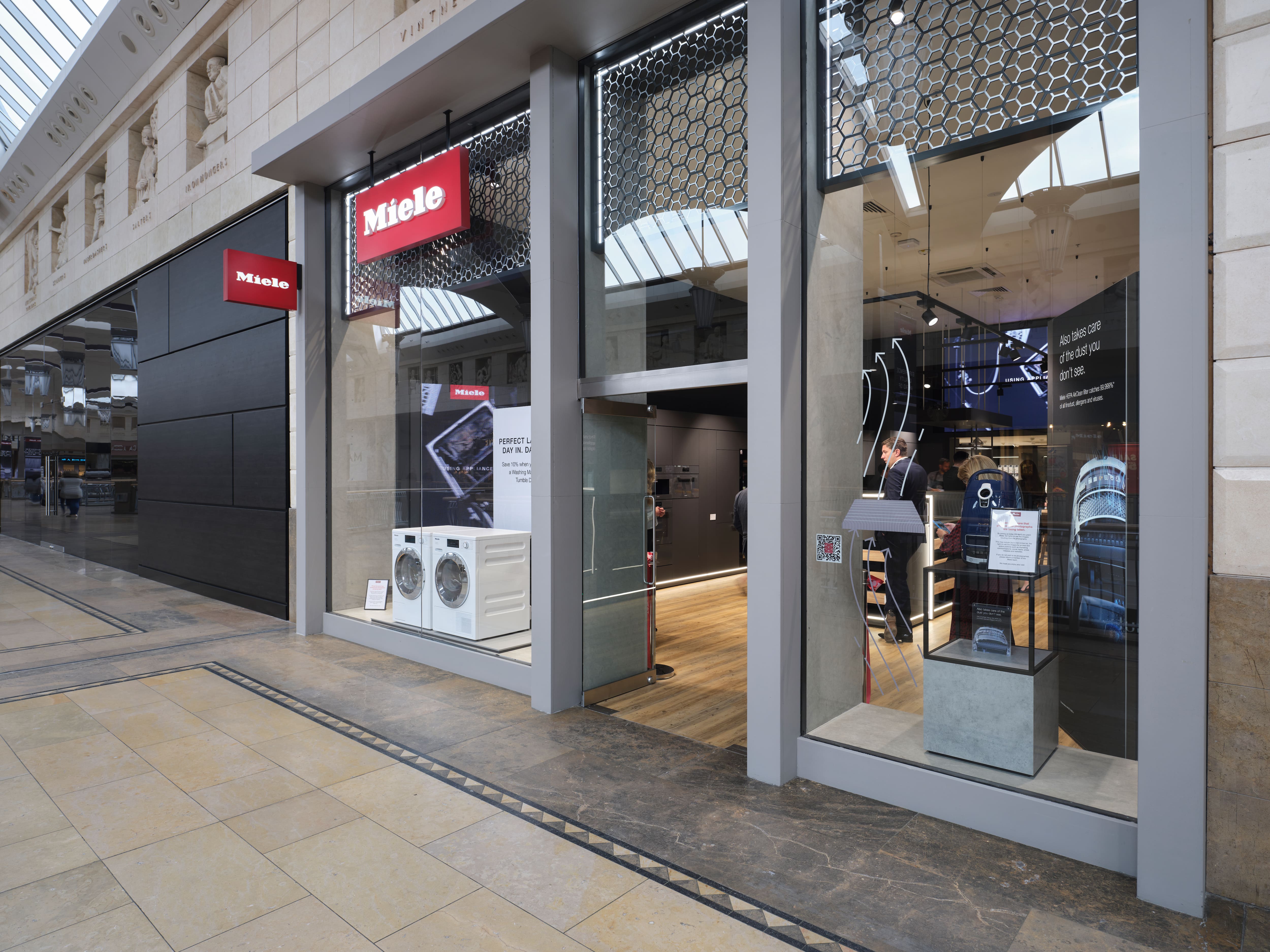 Miele retail storefront in a mall, with washing machines in the window and customers inside exploring. Miele retail storefront in a mall, with washing machines in the window and customers inside exploring.