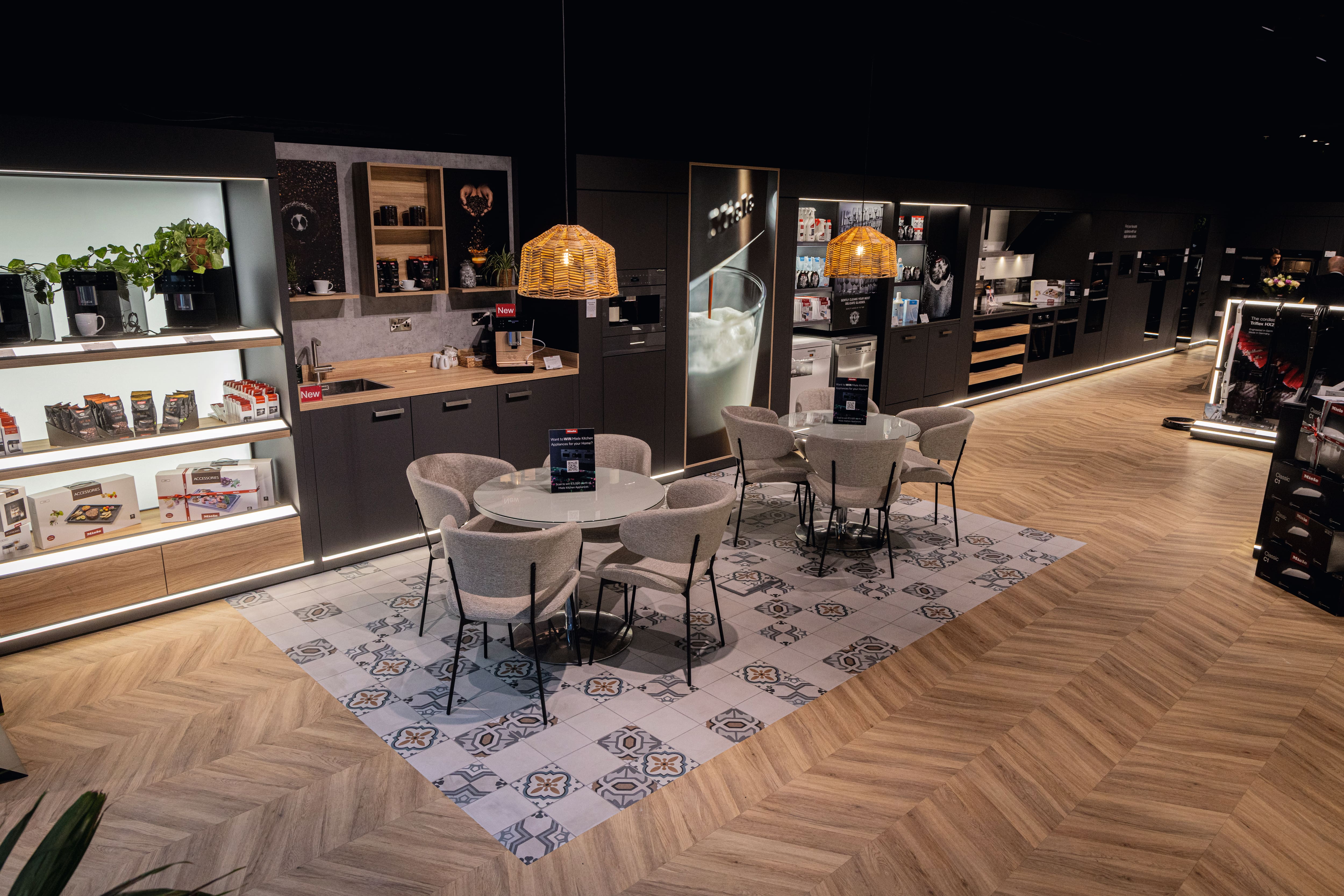 Modern appliance showroom with demo kitchens, coffee machines, and a seating area beneath woven pendant lights. Modern appliance showroom with demo kitchens, coffee machines, and a seating area beneath woven pendant lights.