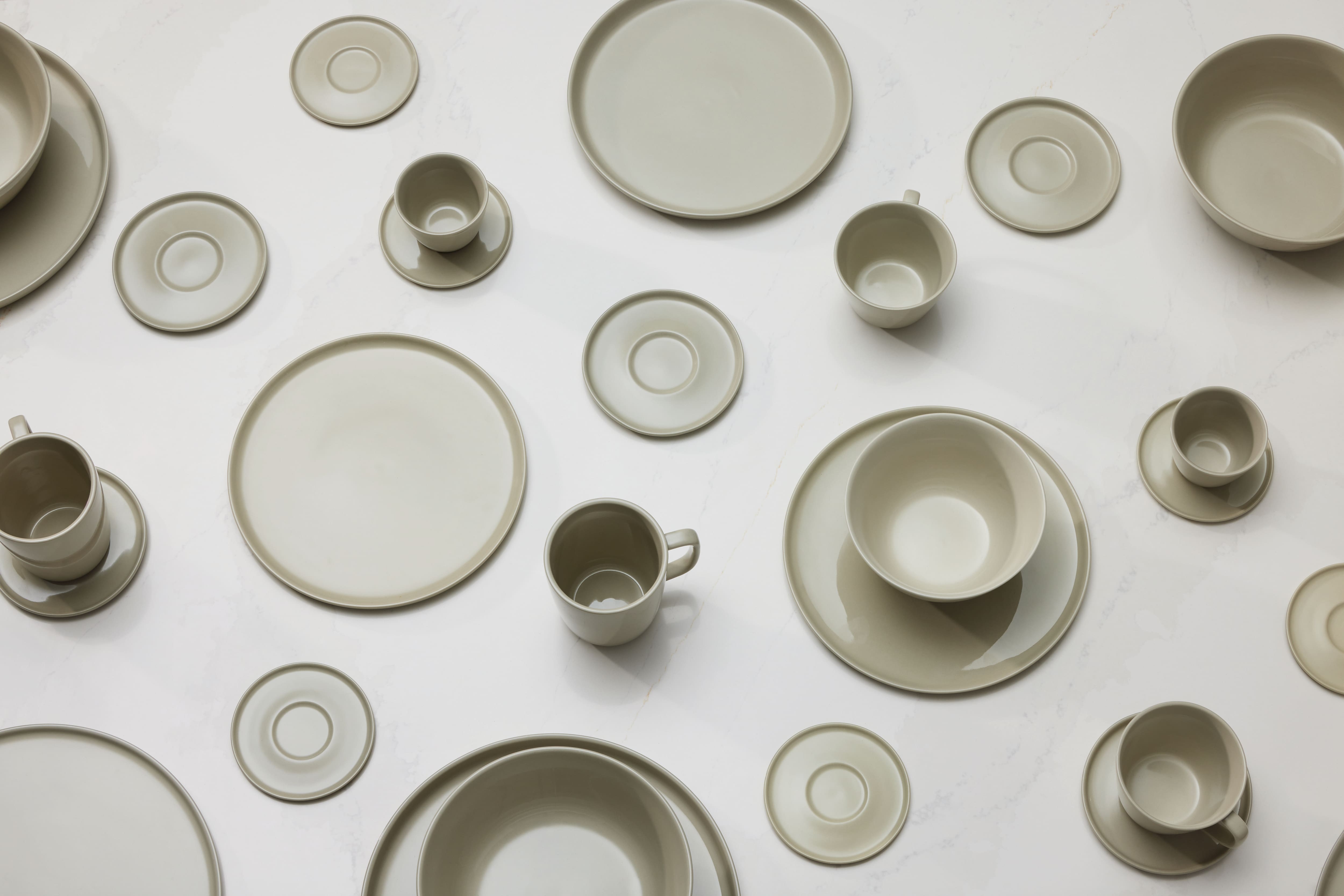 Beige ceramic plates, bowls, cups, and saucers arranged in a clean minimalist flat lay on a white surface.