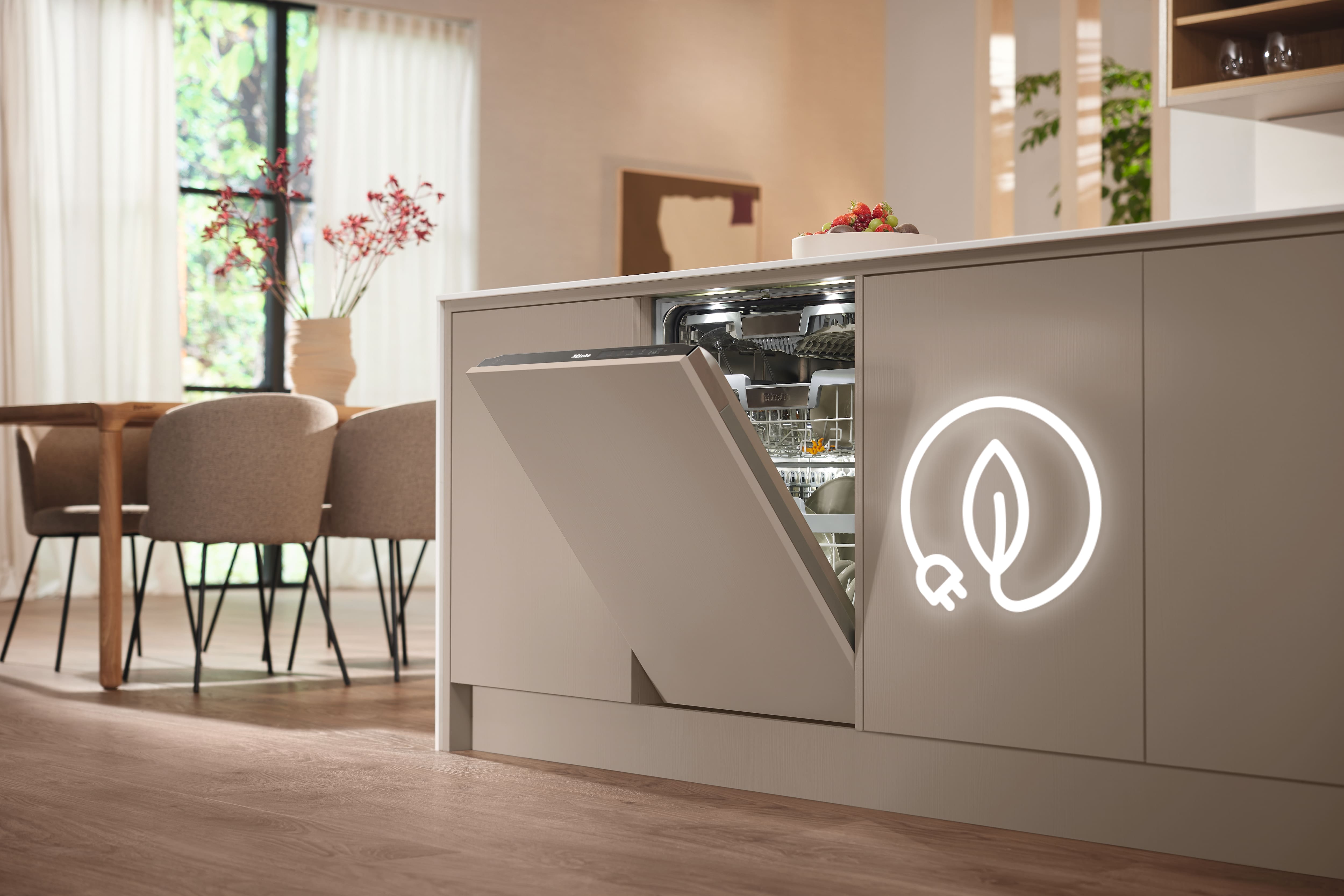Modern kitchen with a built-in dishwasher partially open in a beige island cabinet, interior racks illuminated, and a glowing eco leaf-and-plug symbol on the cabinet; wooden floor, dining table with upholstered chairs, and soft daylight through sheer curtains in the background.