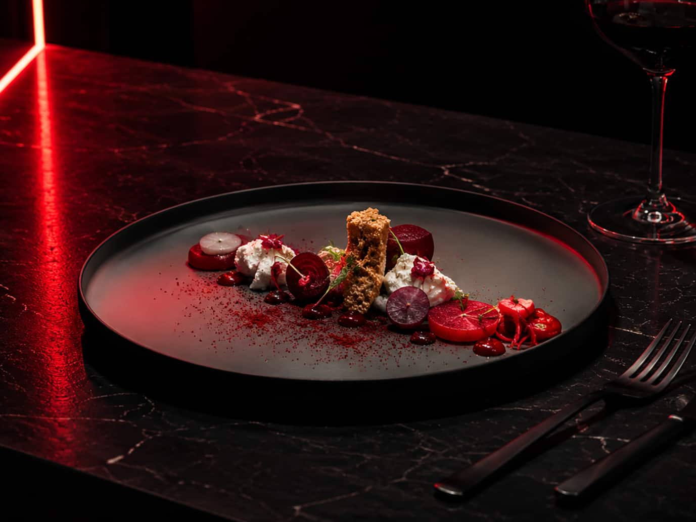 Modern angerichteter Gourmetteller mit Randen (Roter Bete), Käse und knusprigen Bröseln auf dunklem Geschirr. Rote Akzentbeleuchtung, ein Glas Rotwein und eine dunkle Marmoroberfläche schaffen eine elegante Fine-Dining-Atmosphäre. Modern angerichteter Gourmetteller mit Randen (Roter Bete), Käse und knusprigen Bröseln auf dunklem Geschirr. Rote Akzentbeleuchtung, ein Glas Rotwein und eine dunkle Marmoroberfläche schaffen eine elegante Fine-Dining-Atmosphäre.